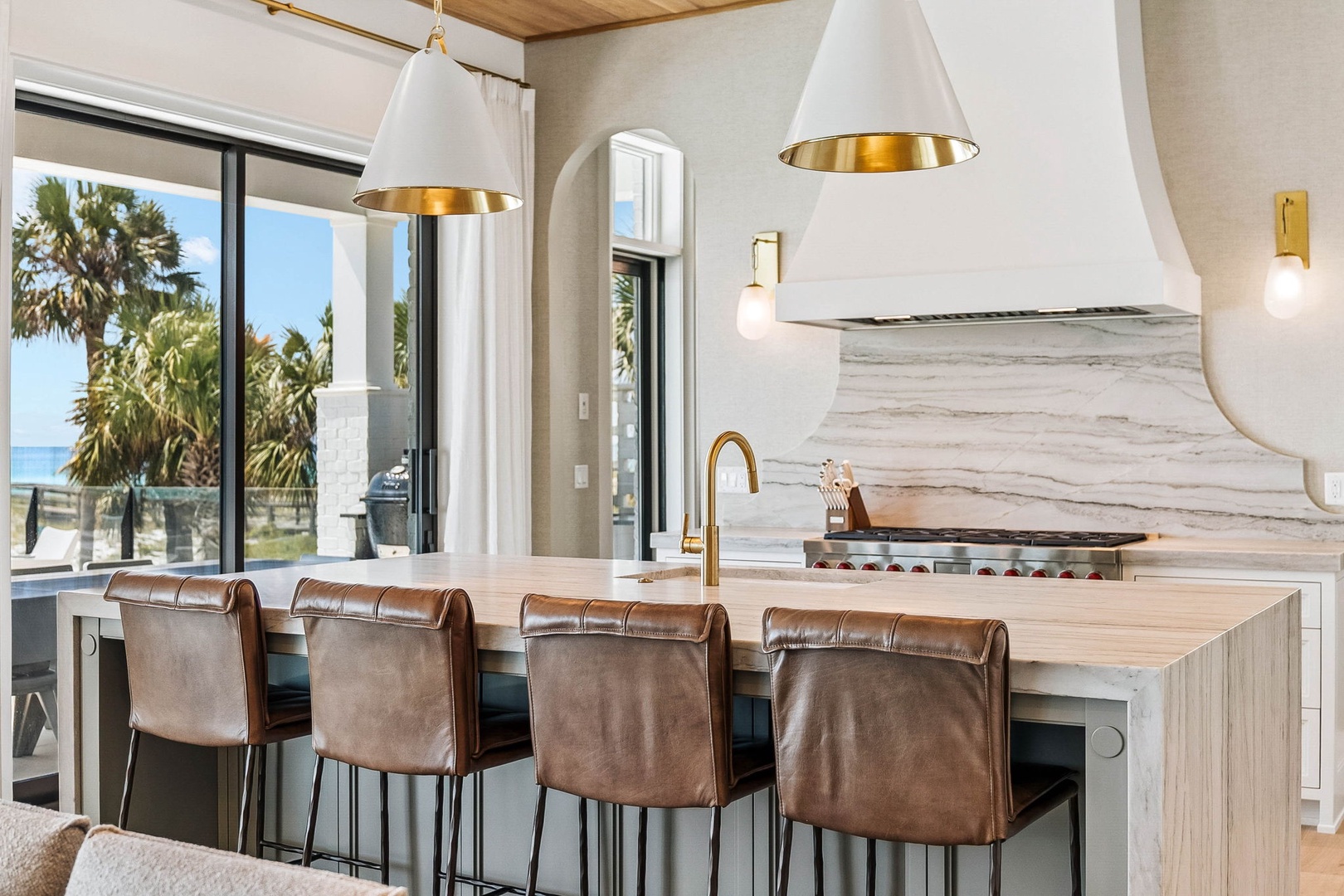 Gather around this stunning kitchen island with ocean views framing your morning coffee. The marble backsplash and warm leather seating invite you to linger over meals while palm trees sway just beyond your window.