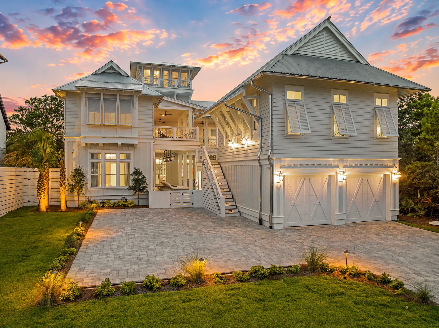 A stunning coastal home bathed in the warm glow of sunset, with elegant white siding and thoughtfully designed outdoor spaces that capture the beauty of the surrounding area.