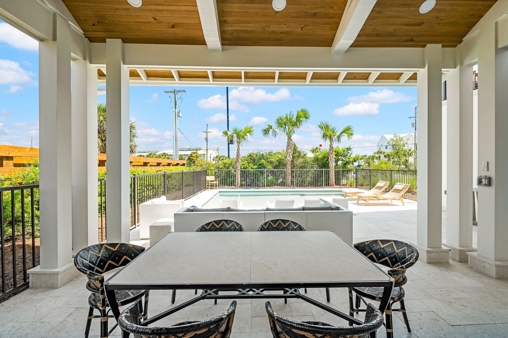 Step into your covered patio where al fresco dining meets modern comfort. Enjoy meals under the wooden ceiling while overlooking the sparkling pool and swaying palms beyond.