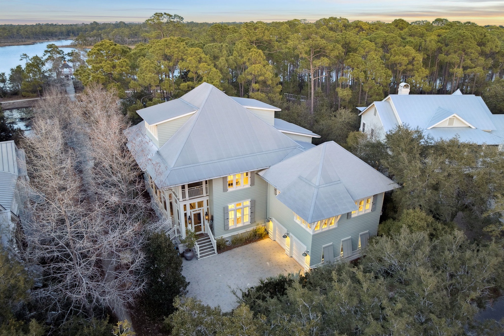 Aerial view of an elegant lakefront property nestled among mature trees with multiple levels and spacious outdoor areas.