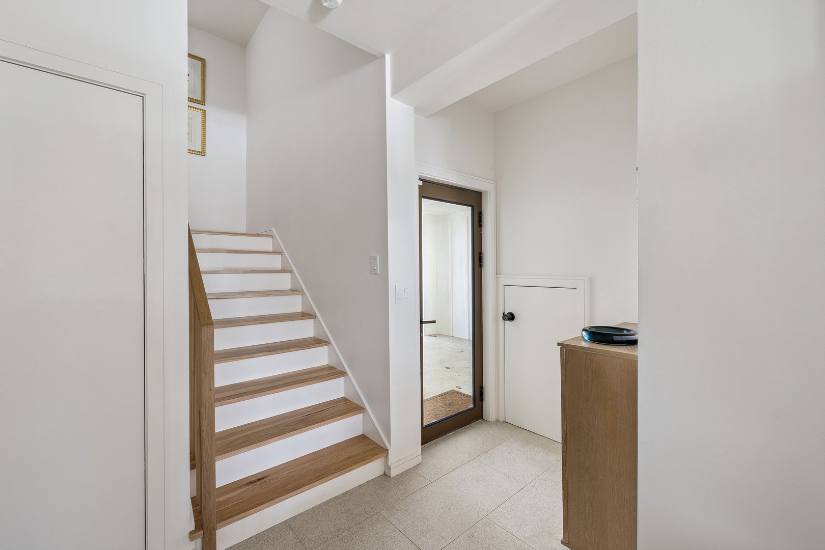 Step into your bright, modern entry featuring warm wood stairs and clean lines throughout the space.