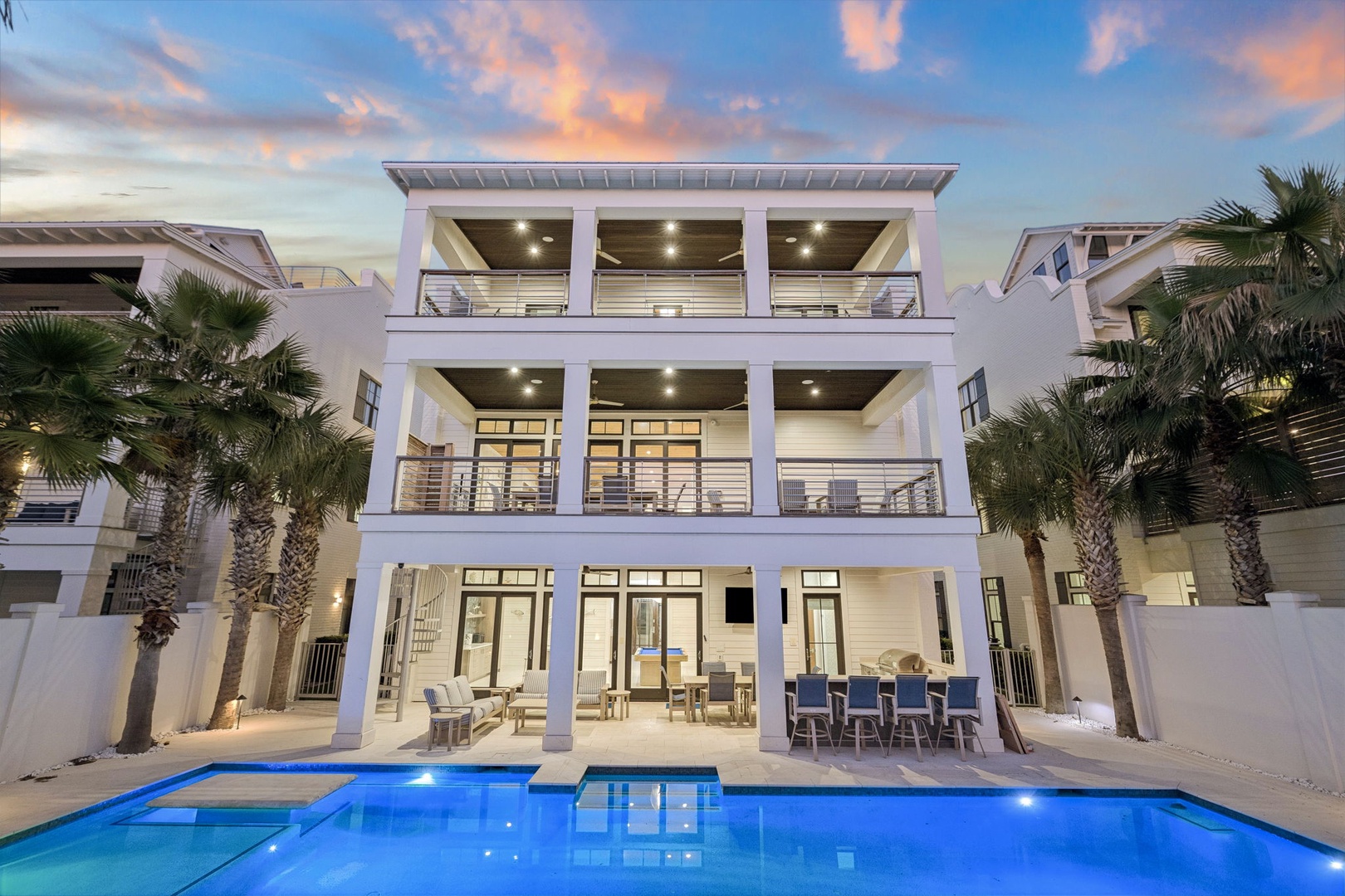 Modern three-story beachside villa with illuminated pool and tropical palms creates an elegant coastal retreat.
