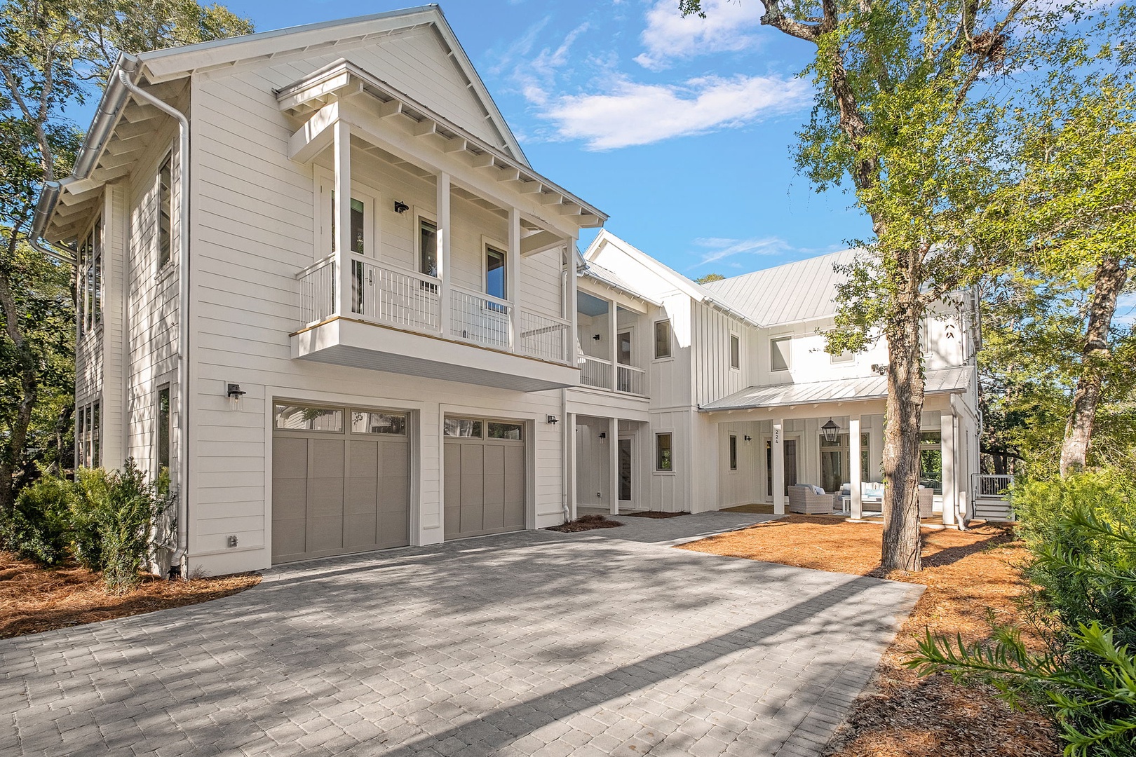 Beautiful white coastal home with spacious driveway and mature trees creating a serene arrival experience.