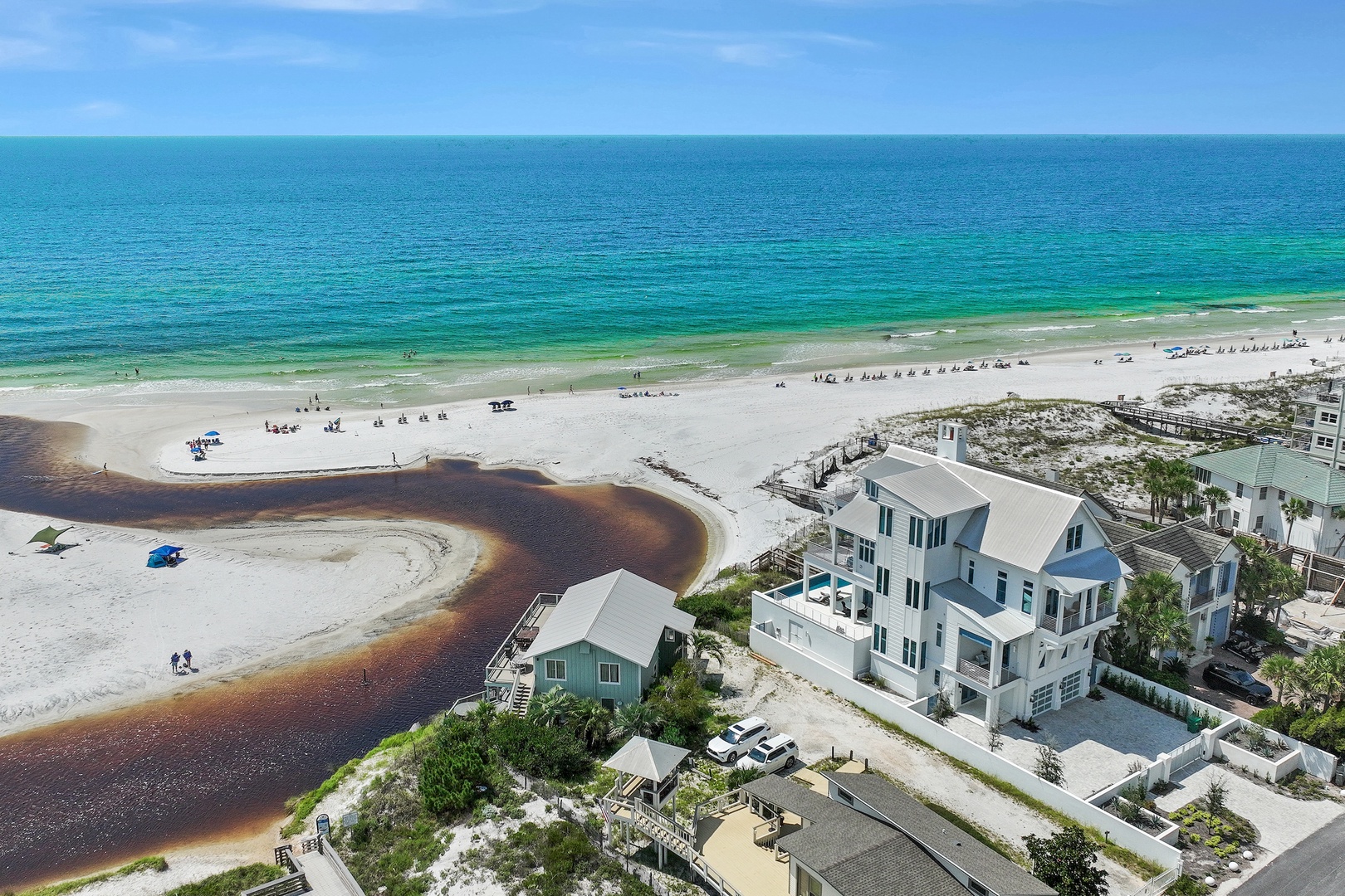 Aerial view of beachfront properties nestled along pristine white sand with emerald Gulf waters stretching to the horizon and a quiet coastal lagoon nearby.