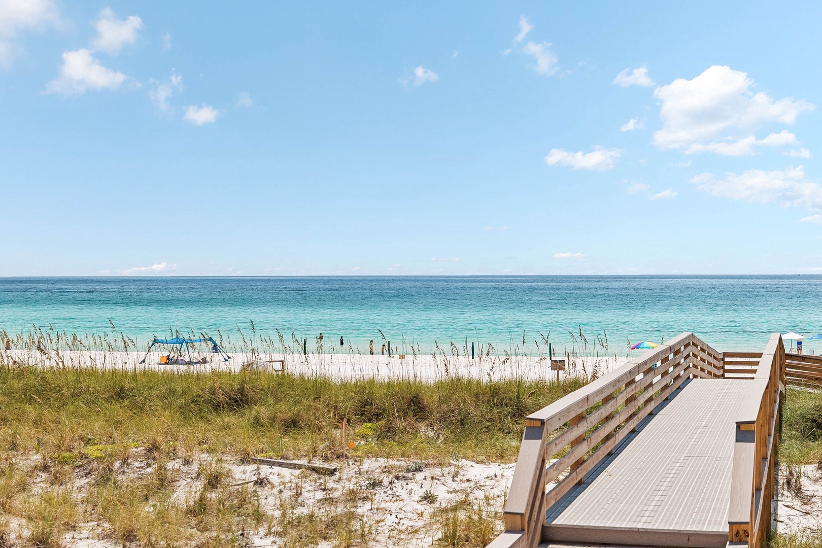 The property offers direct beach access with a wooden boardwalk leading through coastal dunes to pristine white sand and crystal-clear turquoise waters.