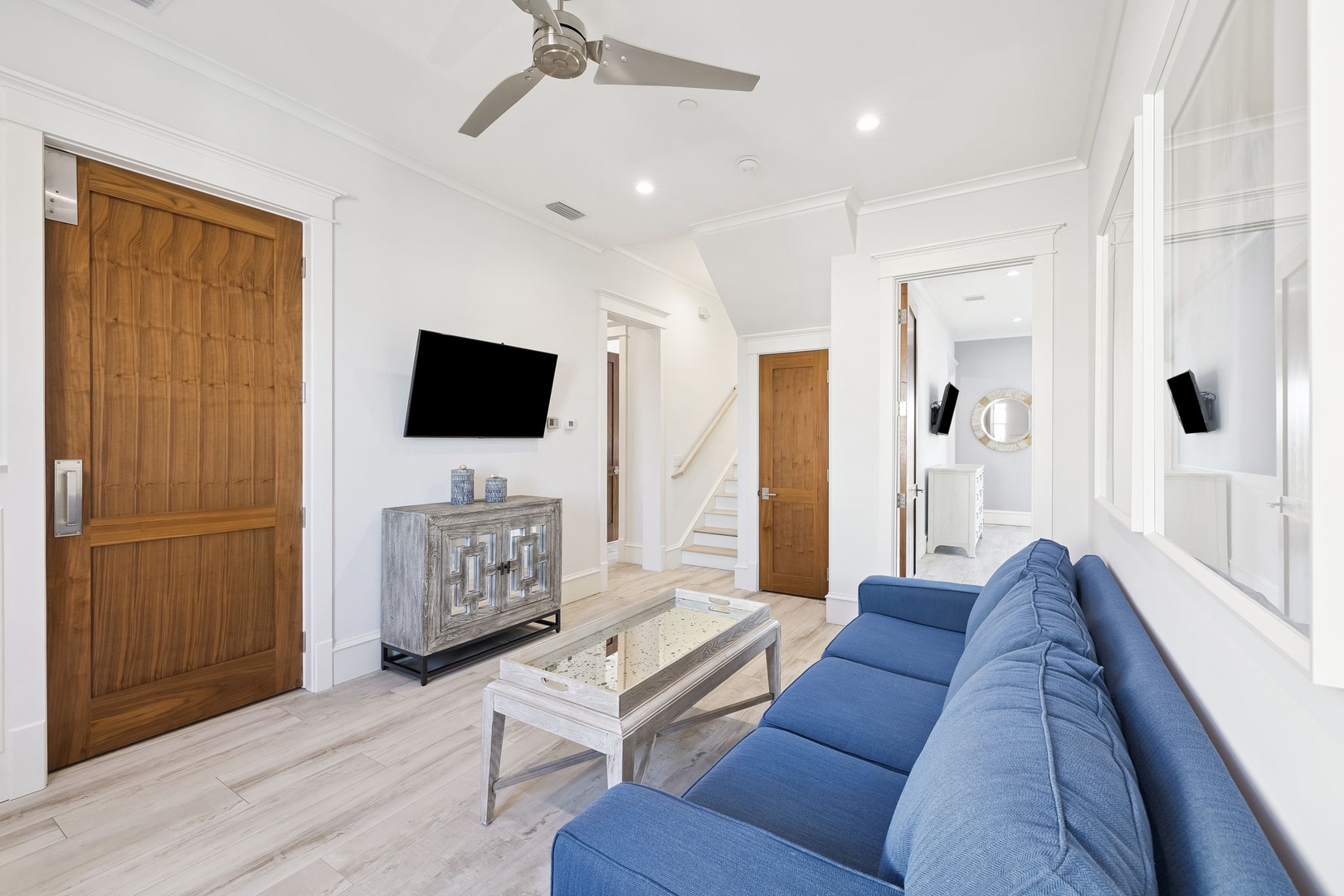 Unwind in your stylish living room with plush blue seating, modern entertainment setup, and soaring ceilings with elegant fan.