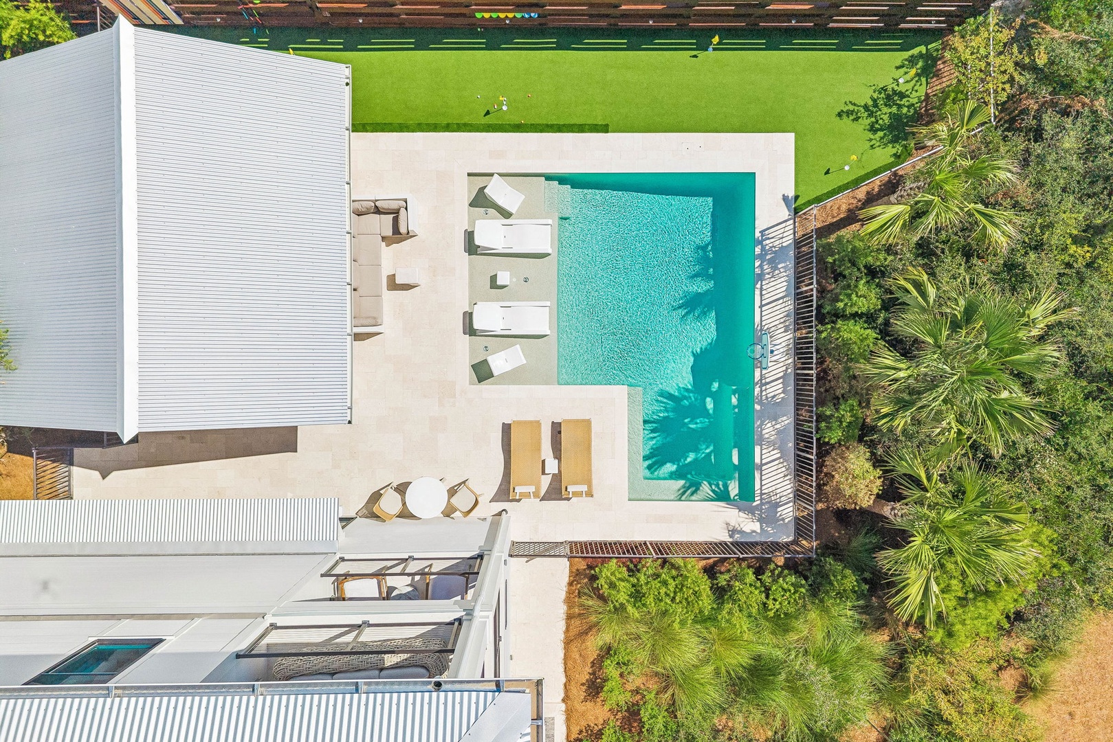 Aerial view of a modern property surrounded by lush tropical landscaping, with a sparkling pool and inviting sunbeds awaiting outdoor relaxation.