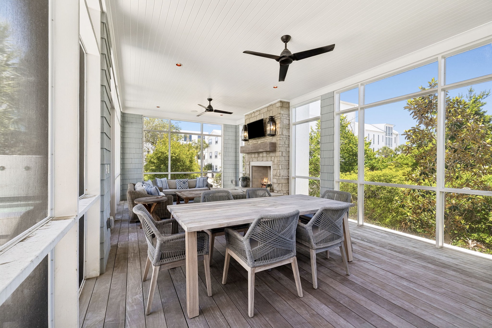 Picture yourself dining here—expansive windows frame lush greenery while ceiling fans cool your evening gatherings. The stone fireplace and cozy seating invite relaxed conversation after meals on your private screened porch.