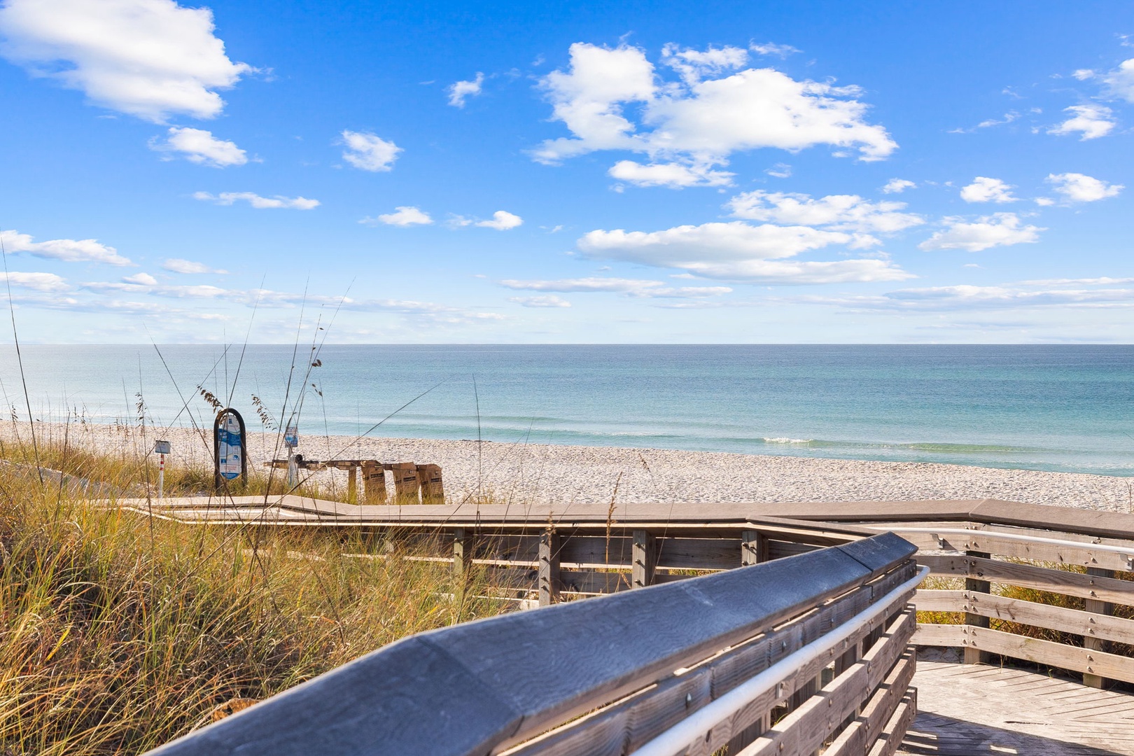 Pristine beach access with wooden boardwalk leading to white sand and crystal-clear waters under beautiful blue skies.