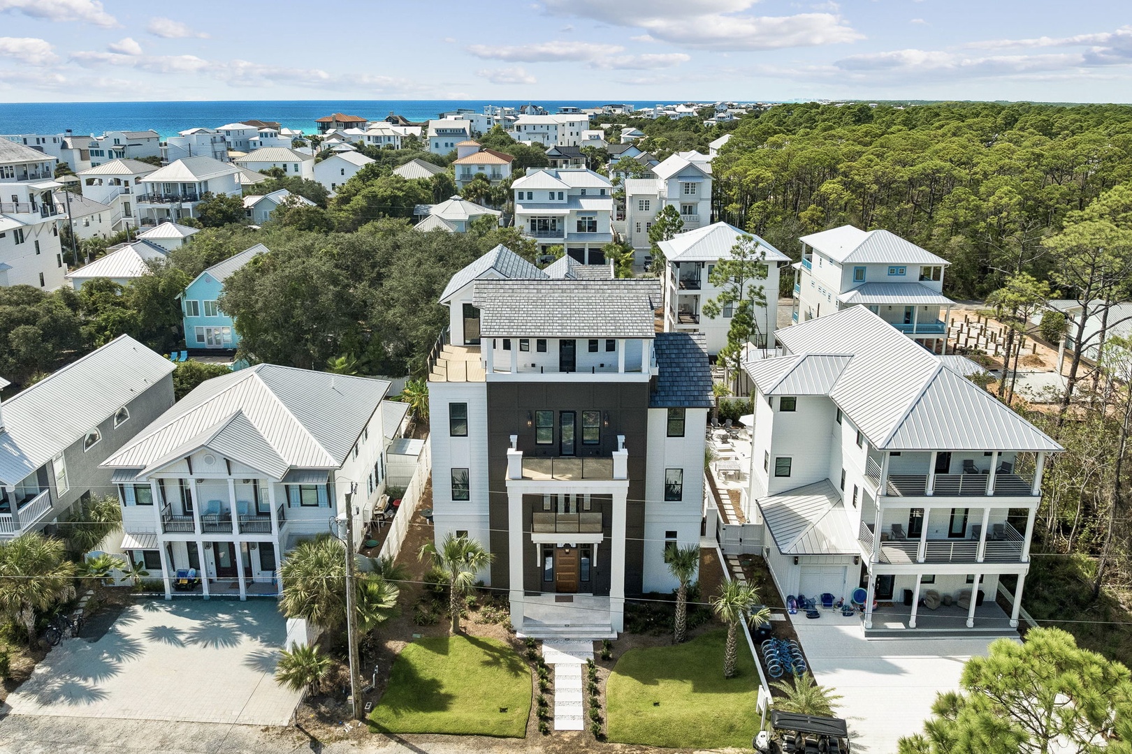 Elevated aerial perspective showcasing the modern coastal property amid lush pine forests and neighboring beach homes, with the turquoise sea visible just beyond this charming Florida community.