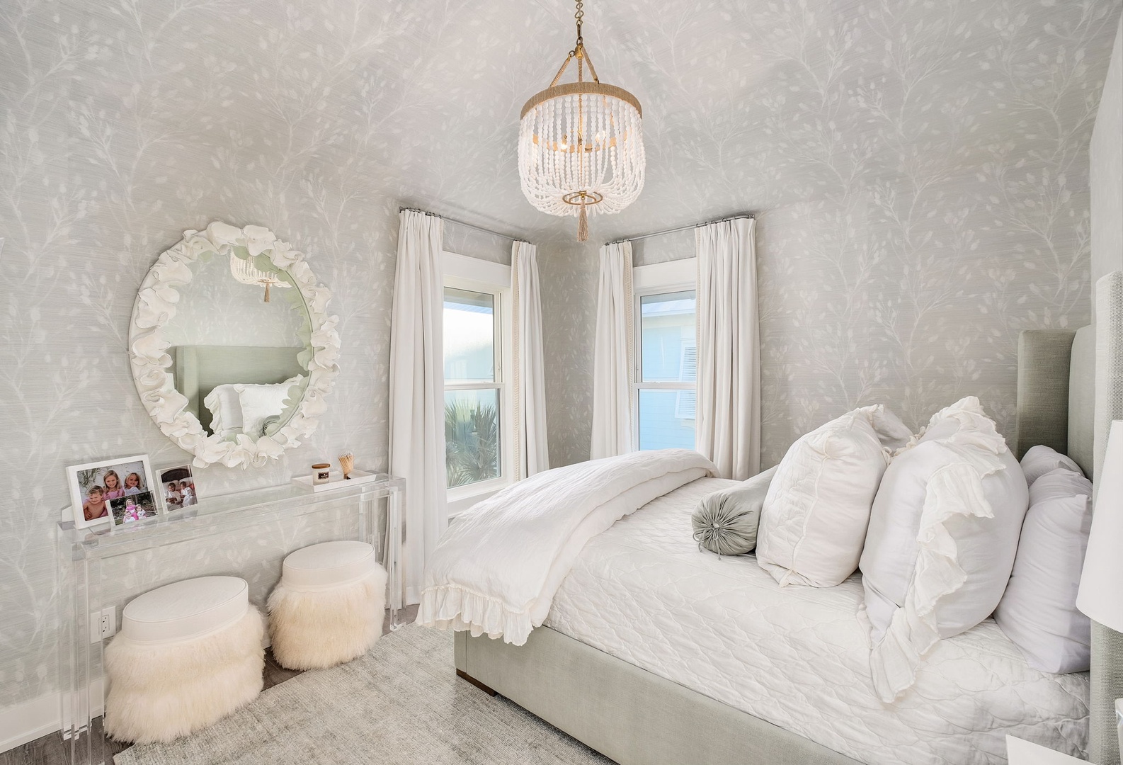 Drift off in this cloud-like retreat with plush linens, a sparkling chandelier, and soft natural light framing serene coastal views.