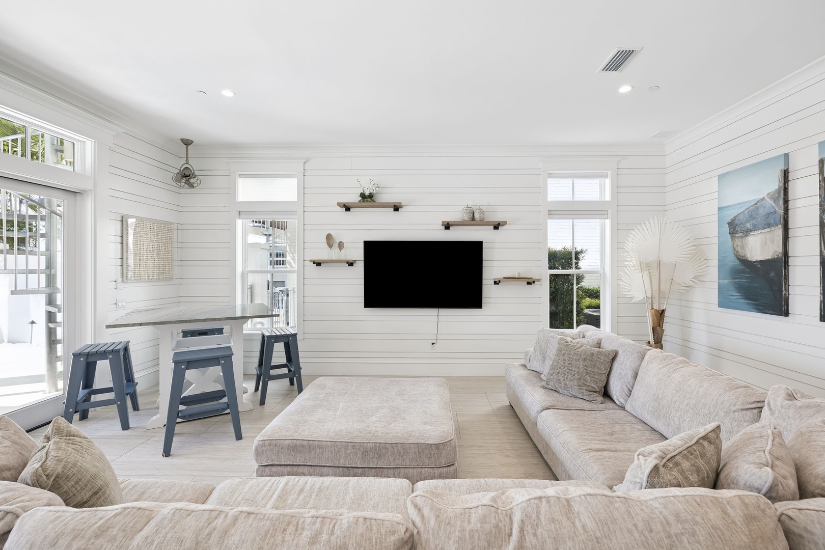 Sink into plush sofas in your bright living space featuring crisp white shiplap walls, floating shelves, and a mounted TV for cozy movie nights.