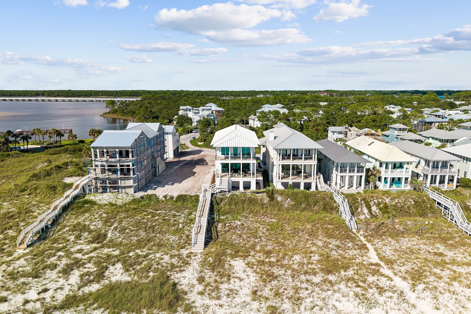 Aerial view of beachfront properties nestled among lush coastal vegetation, with a serene body of water and neighborhood residences visible in the surrounding area.