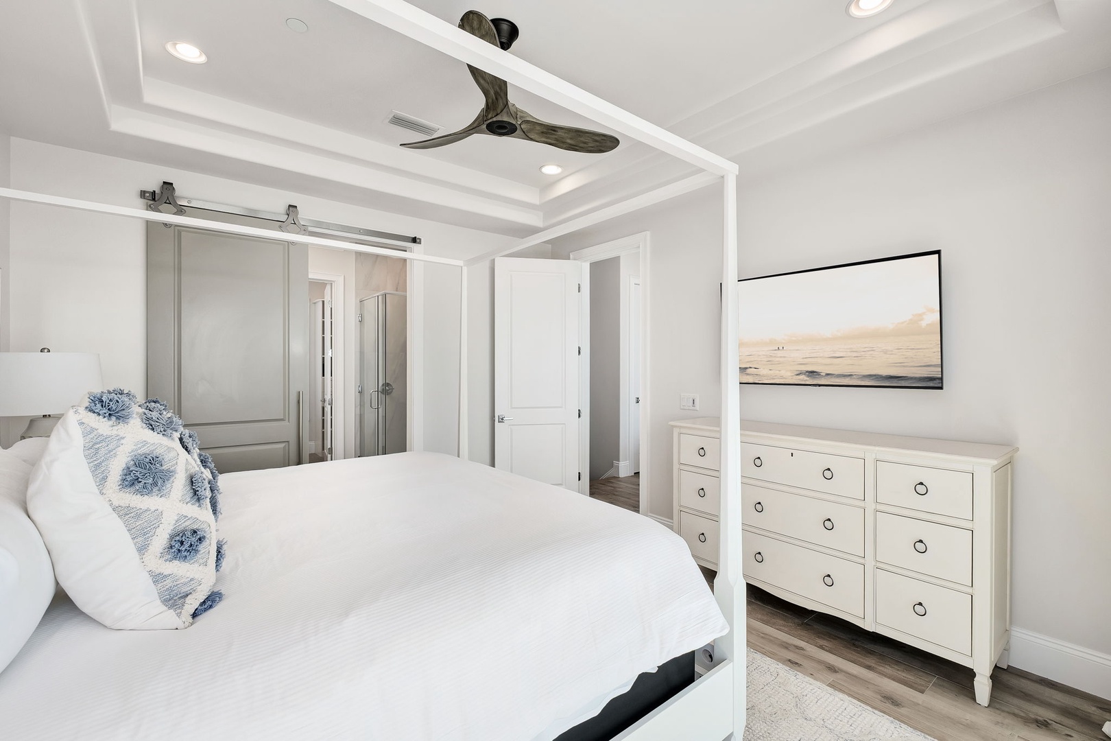 Relax in your serene coastal bedroom with modern coffered ceilings, elegant barn door closets, and peaceful ocean artwork setting the tone for restful nights.