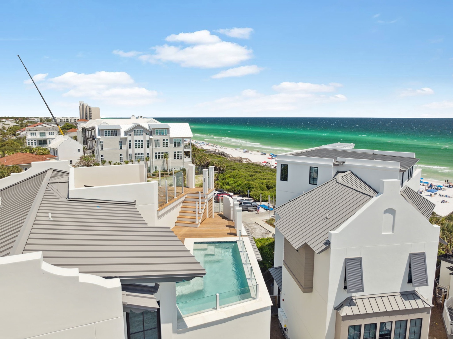 Elevated aerial view showcasing a modern beachfront property with private rooftop pool, situated steps from pristine turquoise Gulf waters and white sand beaches.