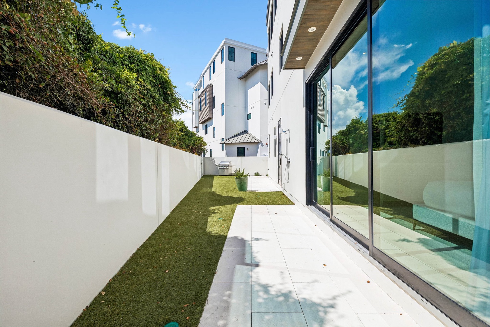 Modern property featuring a sleek, contemporary exterior with floor-to-ceiling glass windows, clean white walls, and a grassy side yard nestled in a quiet residential neighborhood.