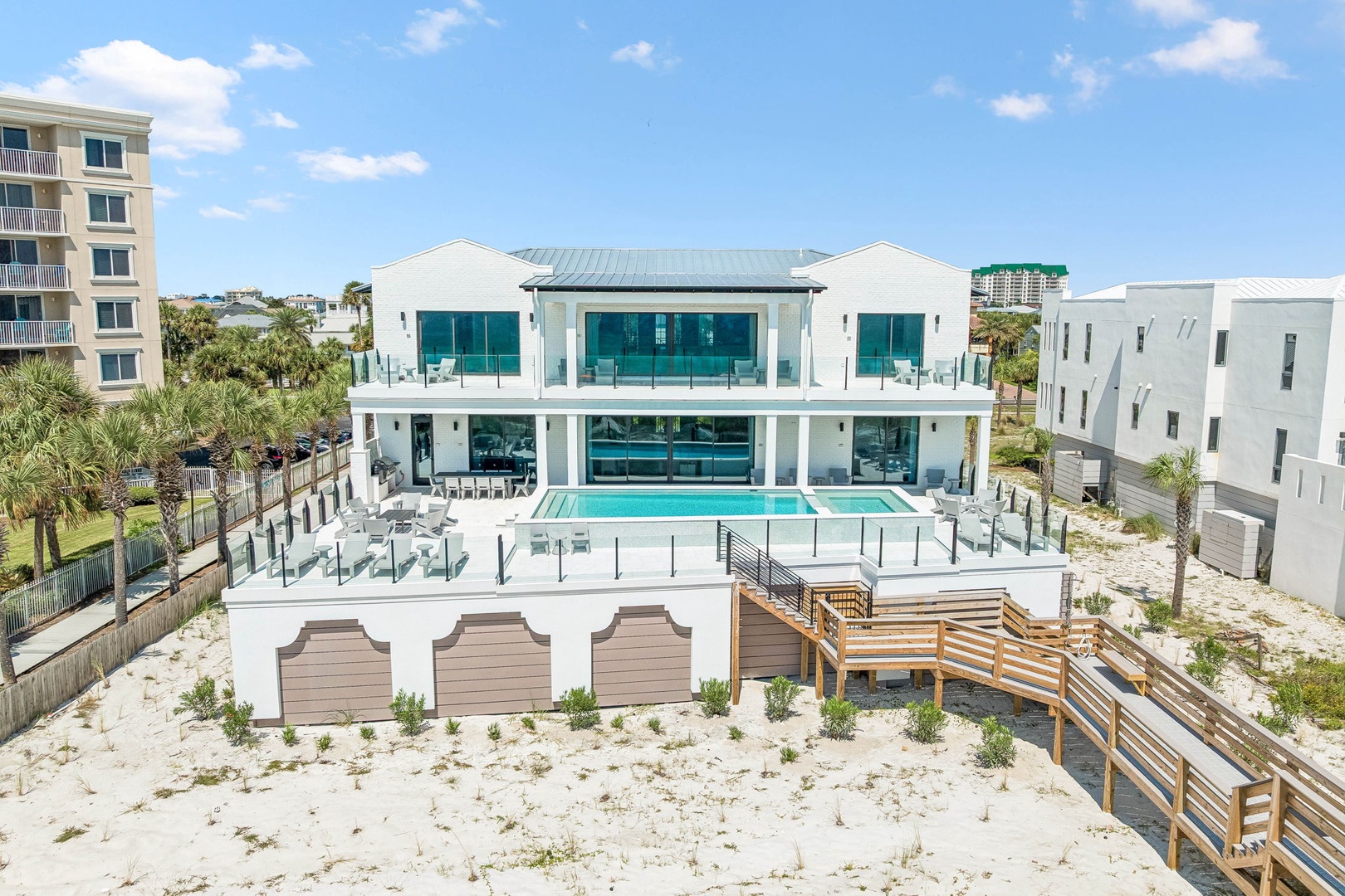 A stunning modern beachfront property with a private pool and direct sand access, surrounded by coastal greenery and neighboring homes.