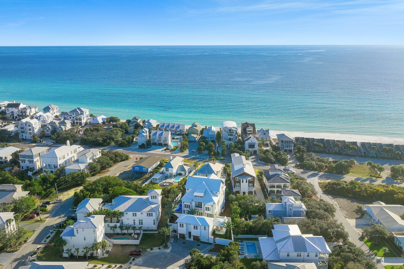 Aerial perspective showcasing a pristine beachfront community with white-sand shores and stunning turquoise waters. This coastal neighborhood features charming beach homes nestled among lush greenery and swaying palms.
