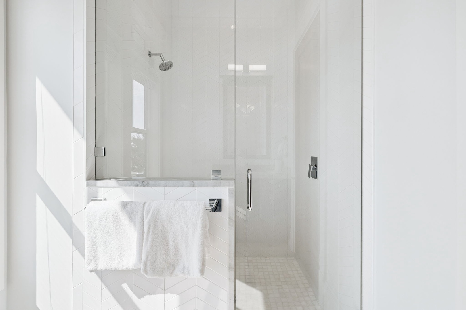 Step into your pristine glass-enclosed shower with rainfall showerhead and marble accents for a luxurious cleansing experience.