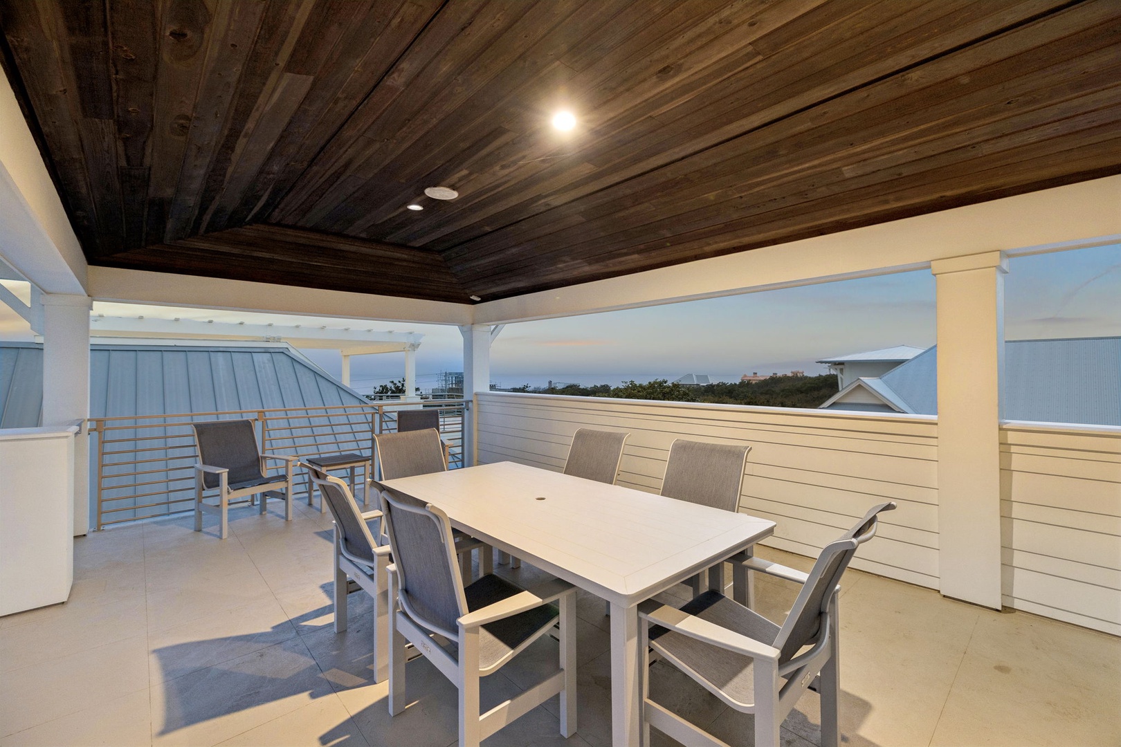 Gather around your private dining table under the warm wood ceiling, where coastal views stretch beyond the modern railings.