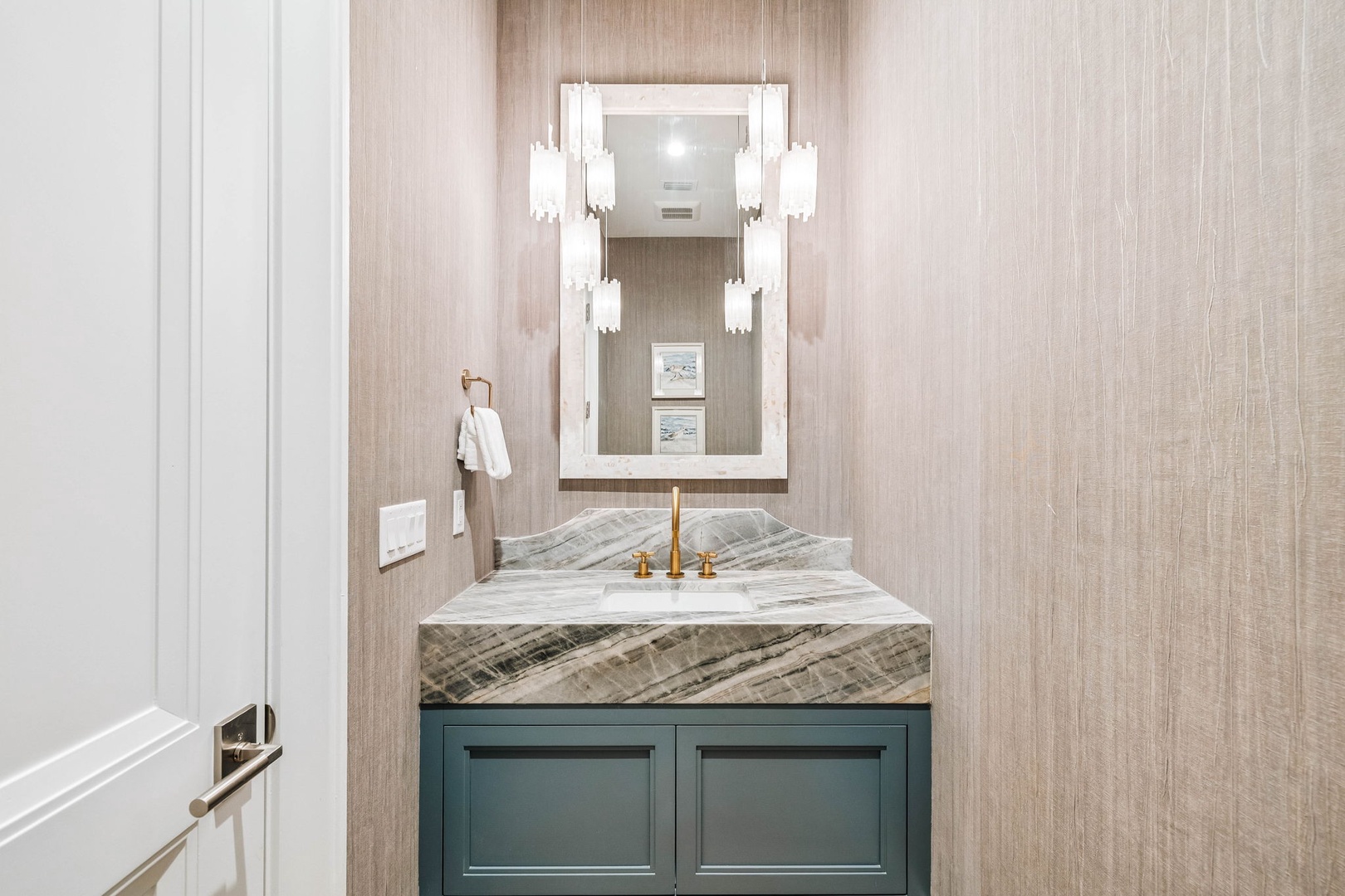 Step into this elegantly appointed powder room, where statement lighting frames a sculptural marble vanity with brass fixtures. The textured wallcovering and crisp white mirror create a sophisticated retreat for your daily routine.