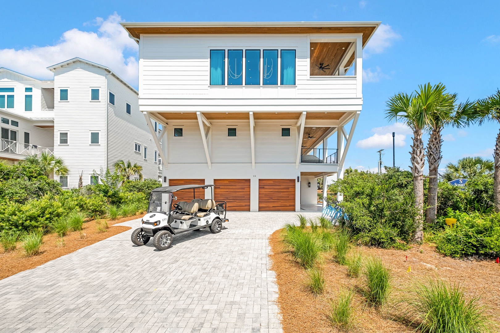 Modern coastal retreat featuring white siding, warm wood accents, and tropical landscaping in a beach neighborhood setting.