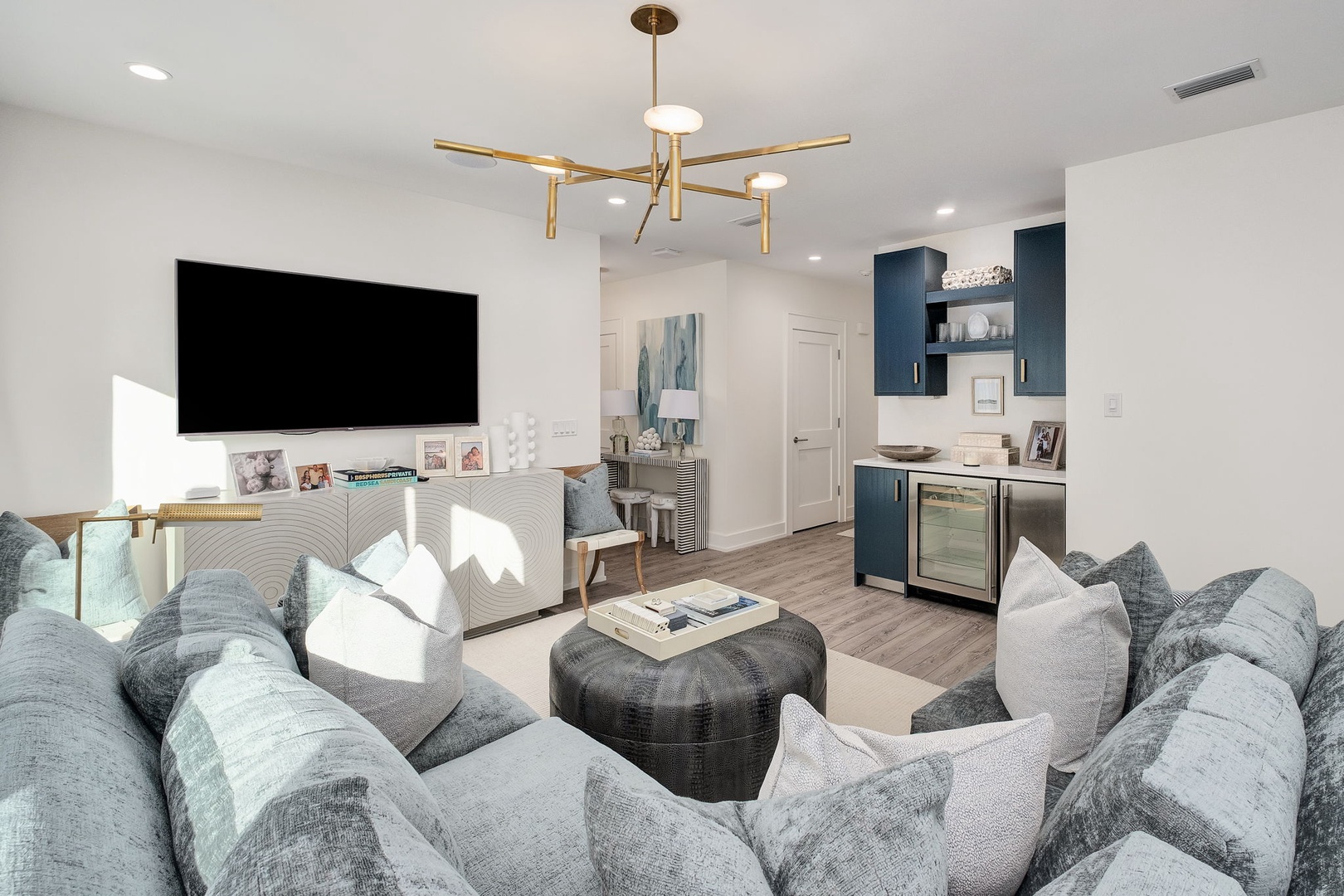Sink into plush seating beneath a modern chandelier as sunlight streams across your open living space, where sleek styling and thoughtful amenities create your perfect retreat.