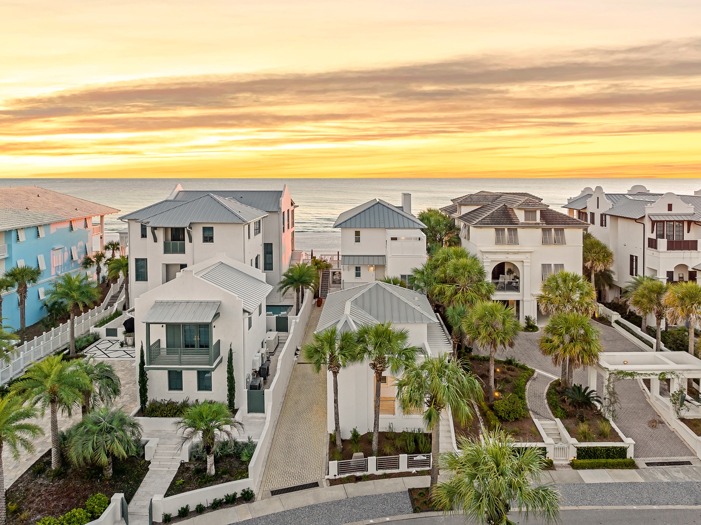 Coastal beachfront neighborhood with modern homes and palm trees beneath a stunning golden sunset sky.