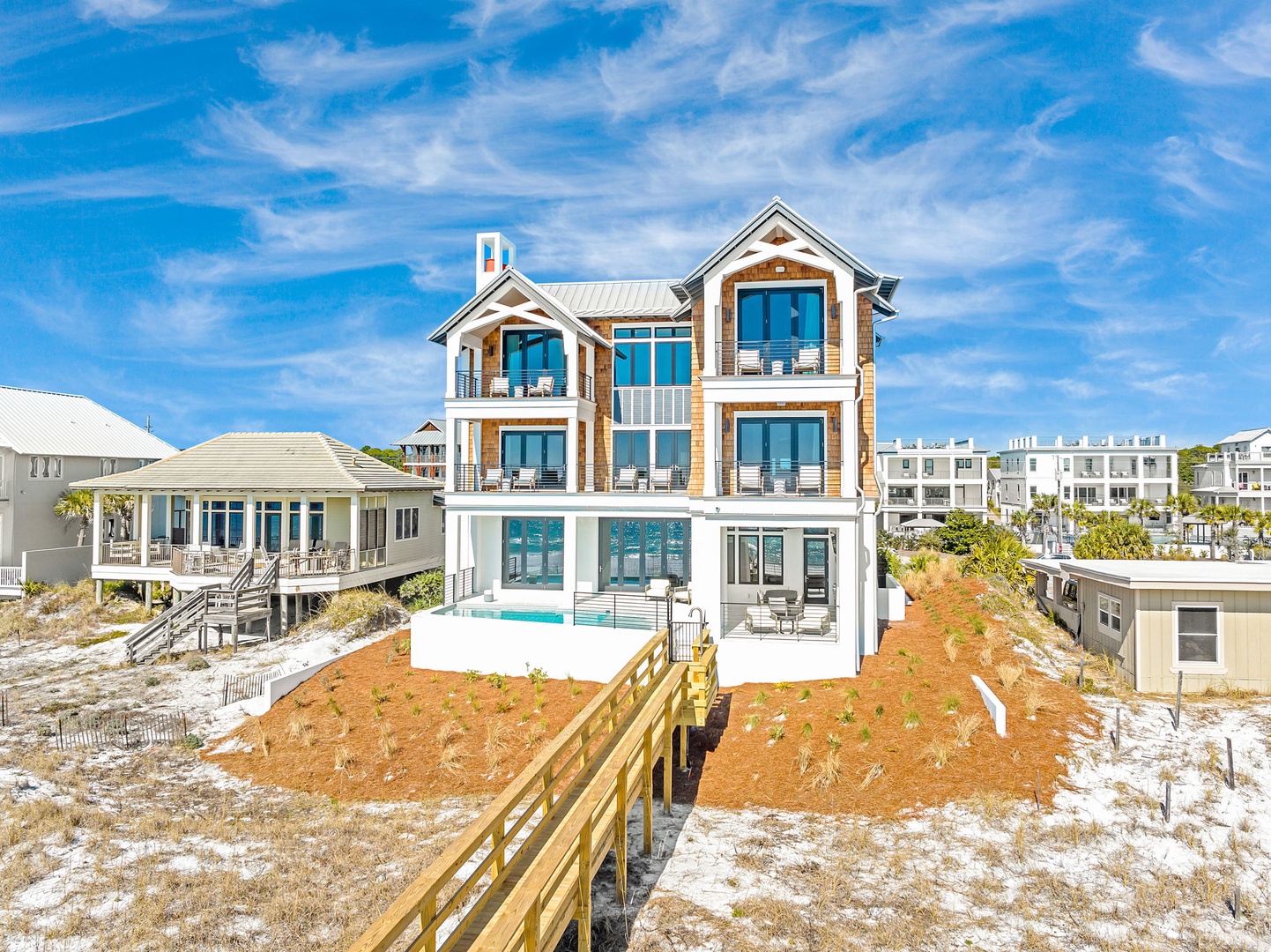 Stunning three-story beachfront property with private pool and boardwalk access, surrounded by coastal dunes and neighboring beach homes.