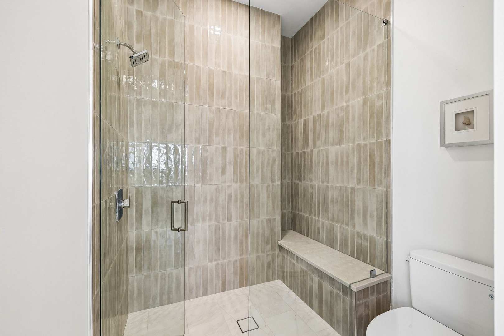 Step into your private spa-like sanctuary, complete with a spacious walk-in shower featuring elegant tilework and a built-in bench for ultimate relaxation.