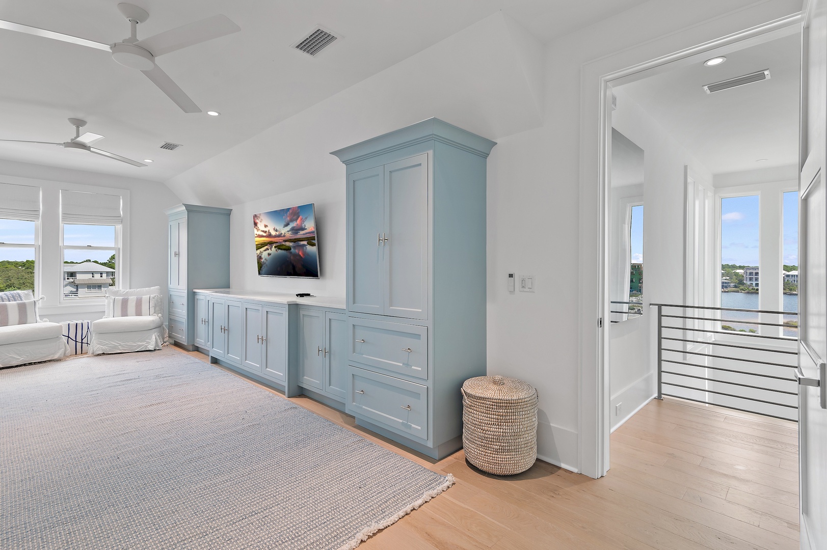 Relax in your bright, airy bedroom with coastal-blue built-ins and serene water views. Natural light floods through white-framed windows as ceiling fans keep you comfortable.