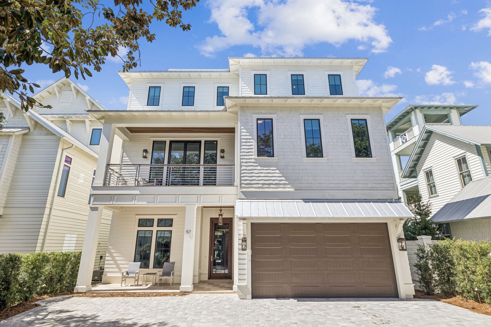 Modern three-story coastal home with elegant white exterior, featuring covered balcony and welcoming front entrance in charming neighborhood setting.