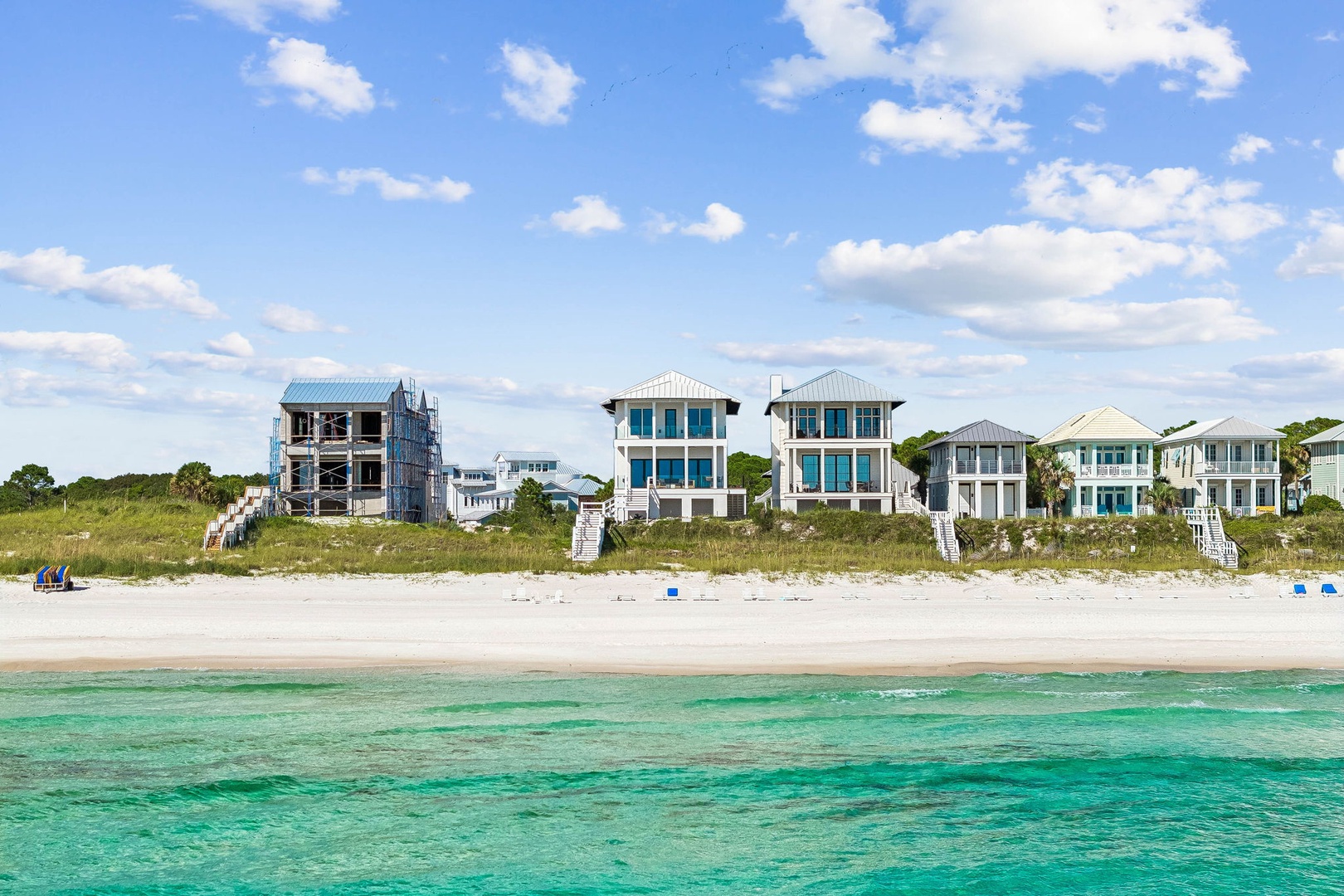 Beachfront properties with direct access to pristine white sand and crystal-clear turquoise waters, surrounded by natural dune vegetation and swaying palms.
