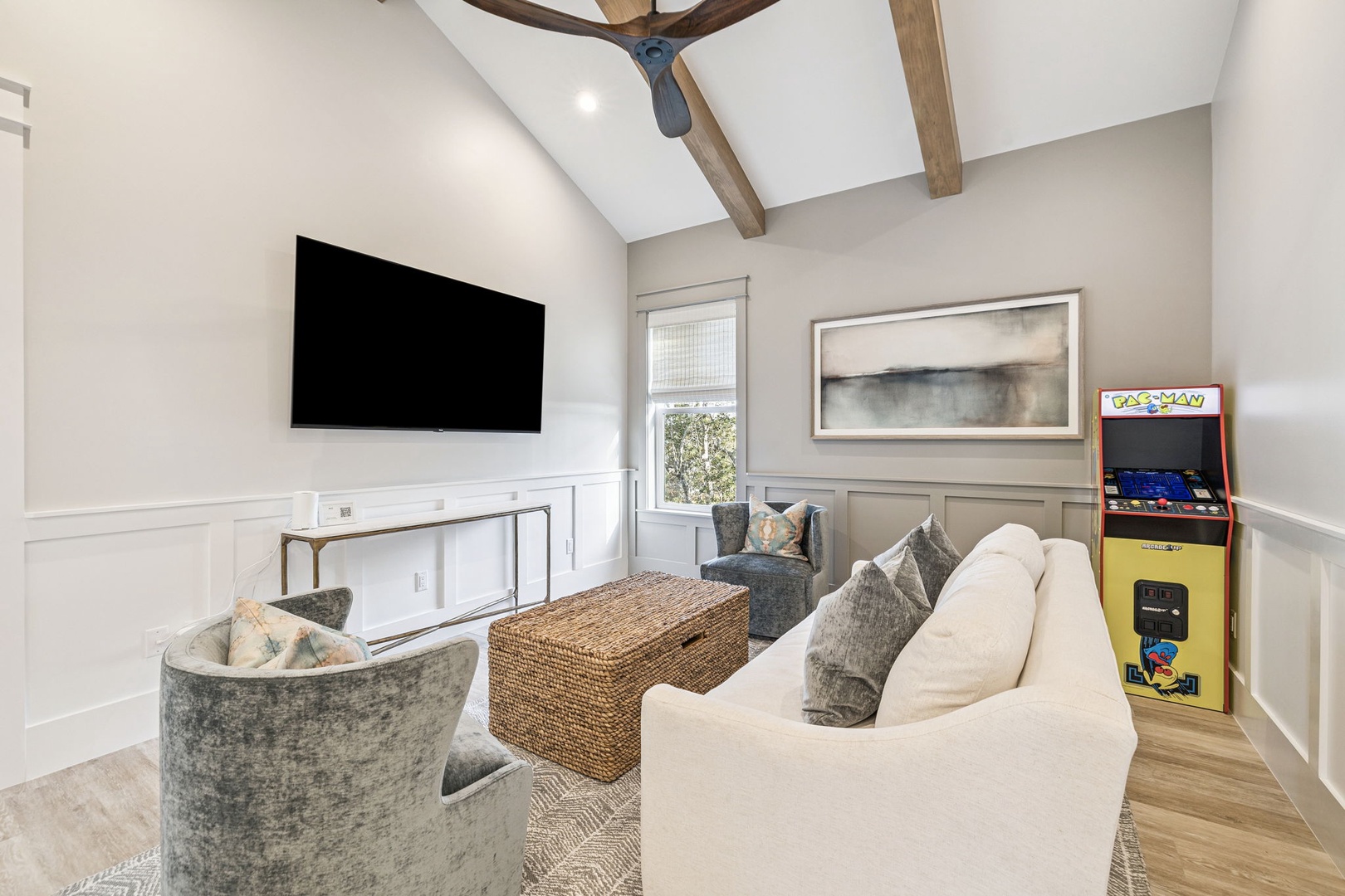 Relax in your stylish entertainment space featuring exposed wood beams, plush seating, and a classic arcade game for hours of fun.