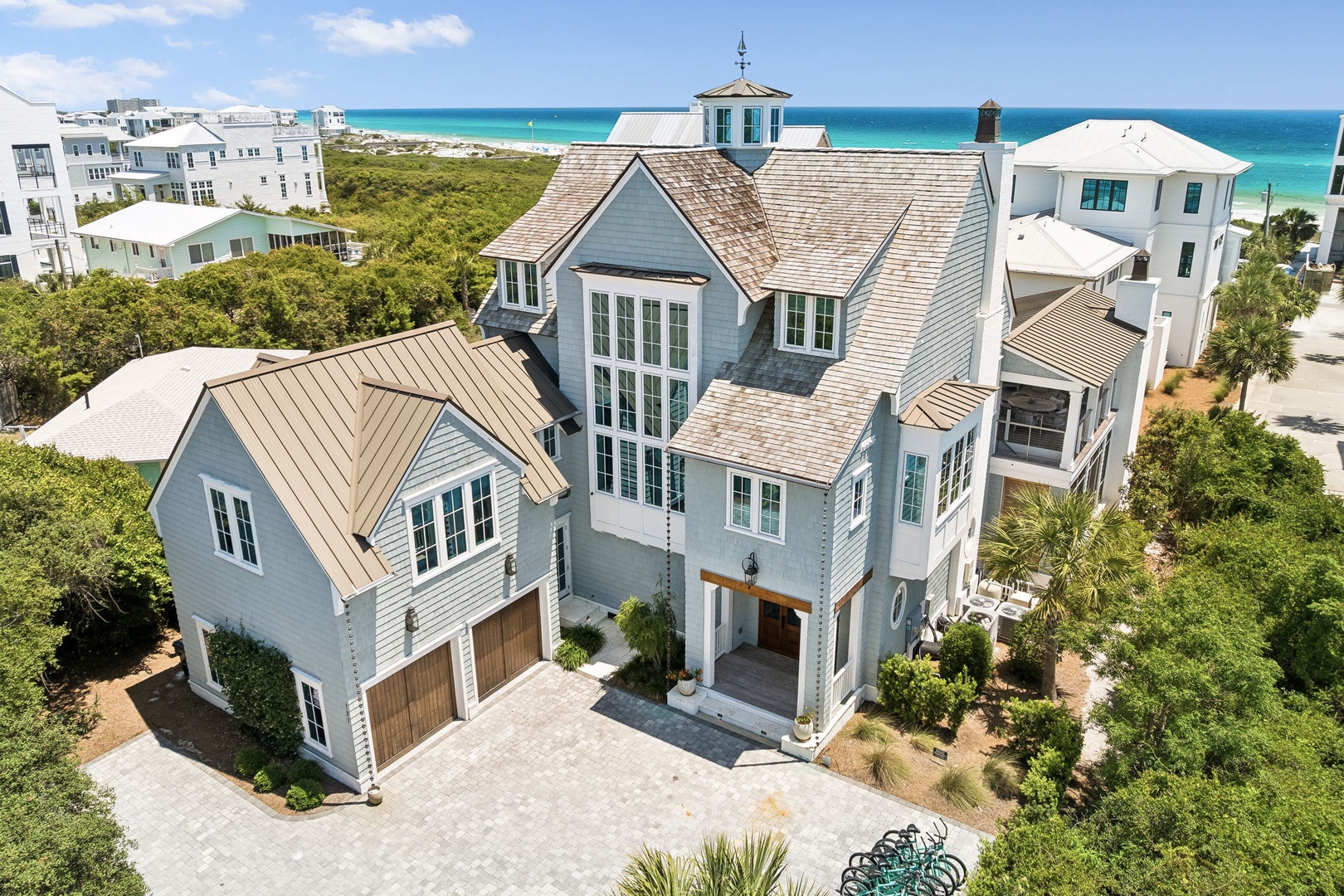 Stunning coastal property with beach access, nestled among lush greenery and surrounded by beautiful neighboring homes. The architecture features elegant rooflines and a spacious driveway.