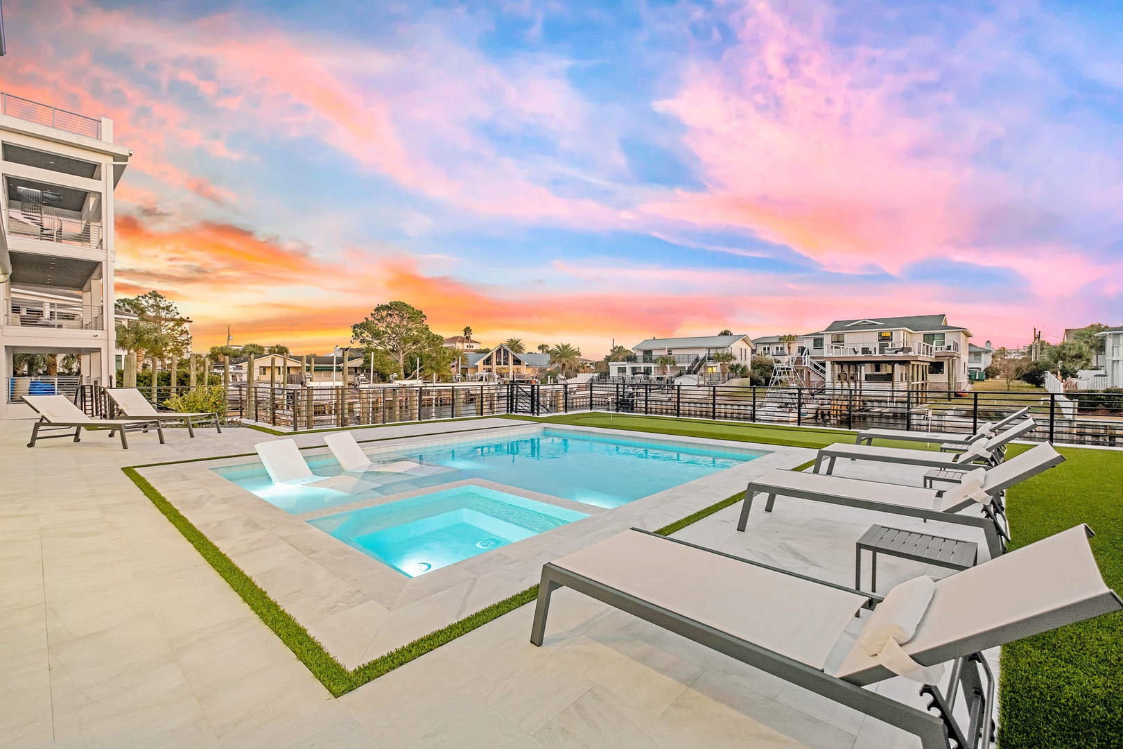 Stunning sunset paints the sky in vibrant colors above this modern coastal community, featuring a pristine pool and spa area.