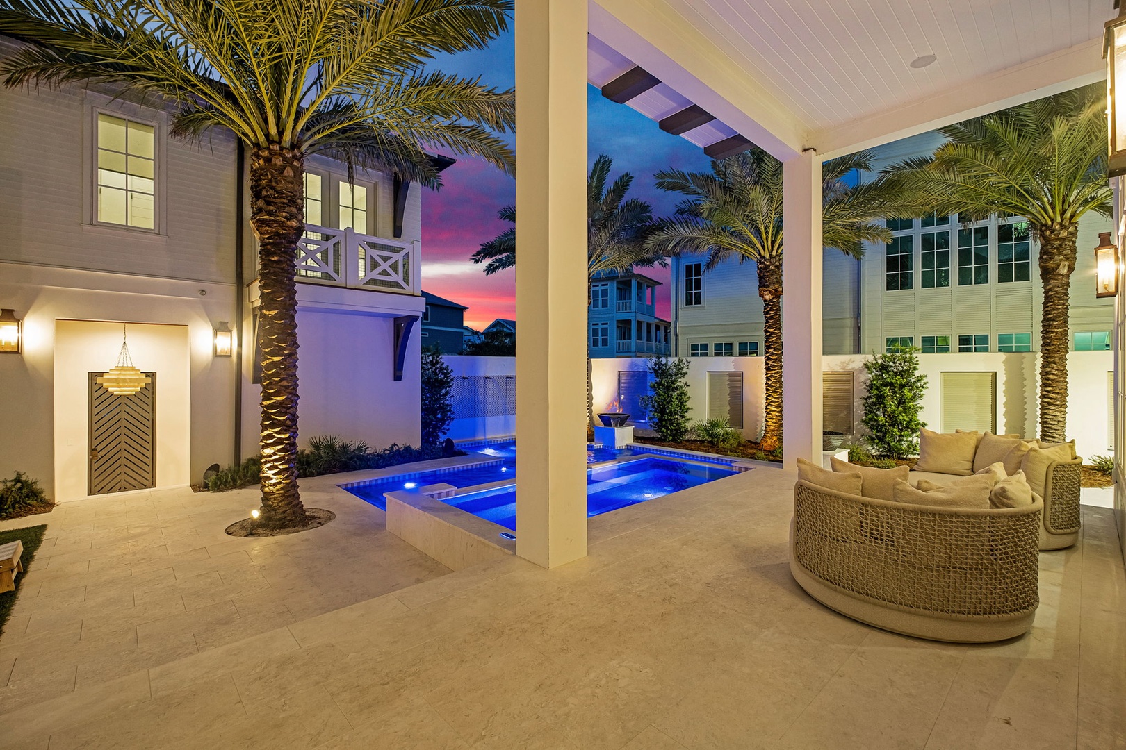 A stunning courtyard oasis framed by palm trees and bathed in the glow of a breathtaking sunset, where the elegantly illuminated pool and inviting outdoor seating create the perfect backdrop for your evening unwind.