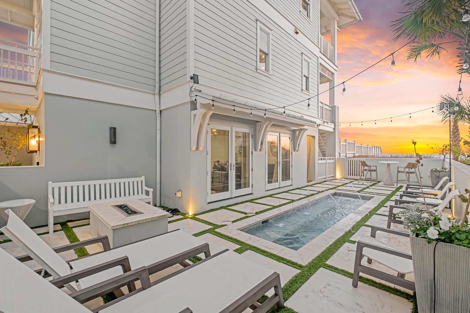 A luxurious outdoor retreat with a private pool and lounge chairs, framed by string lights and a stunning sunset—perfect for unwinding after a day at the beach.