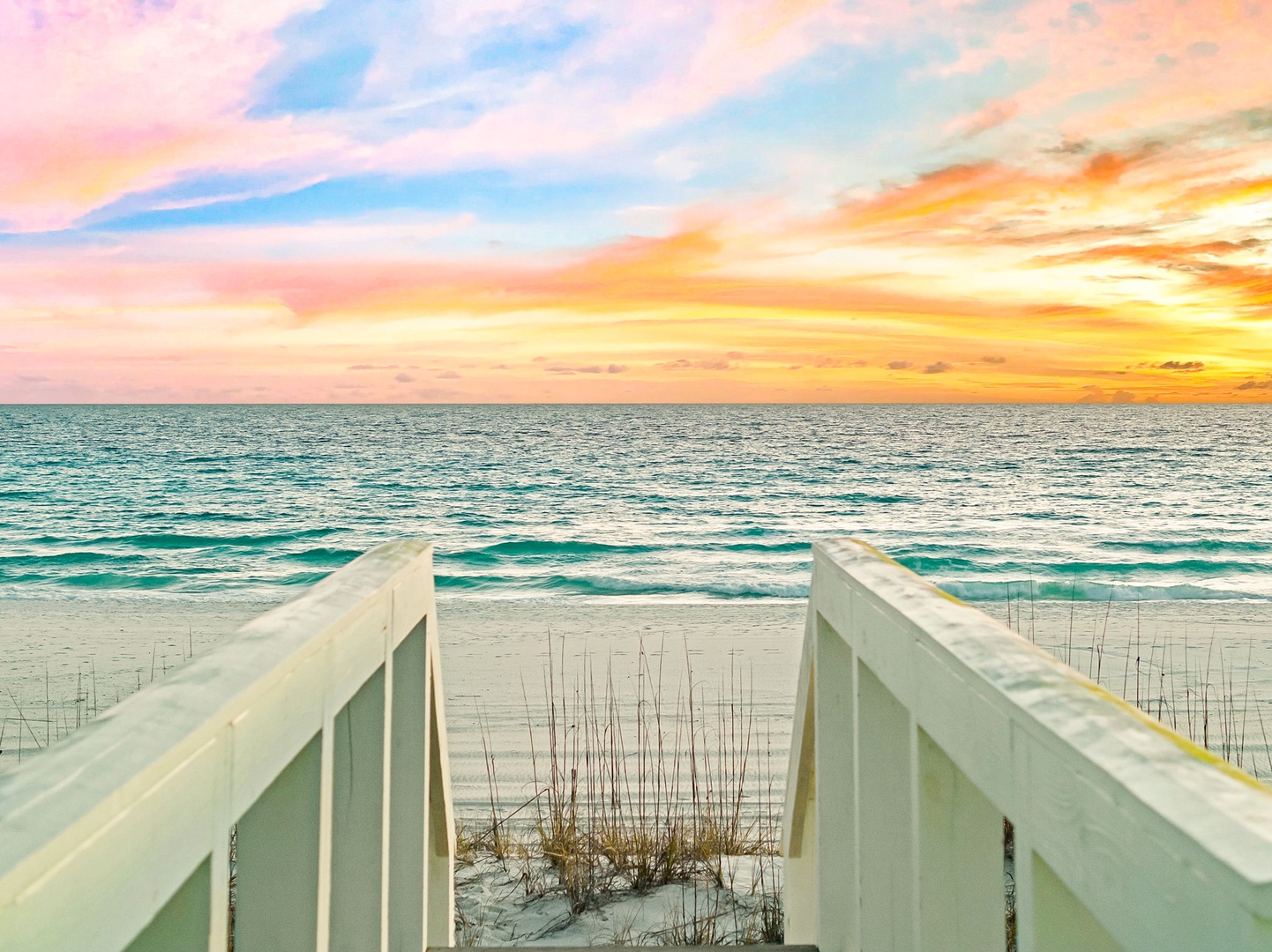 A private walkway leads directly to pristine white sand beaches and turquoise waters, framed by a breathtaking sunset painting the sky in soft pinks, blues, and golden hues.