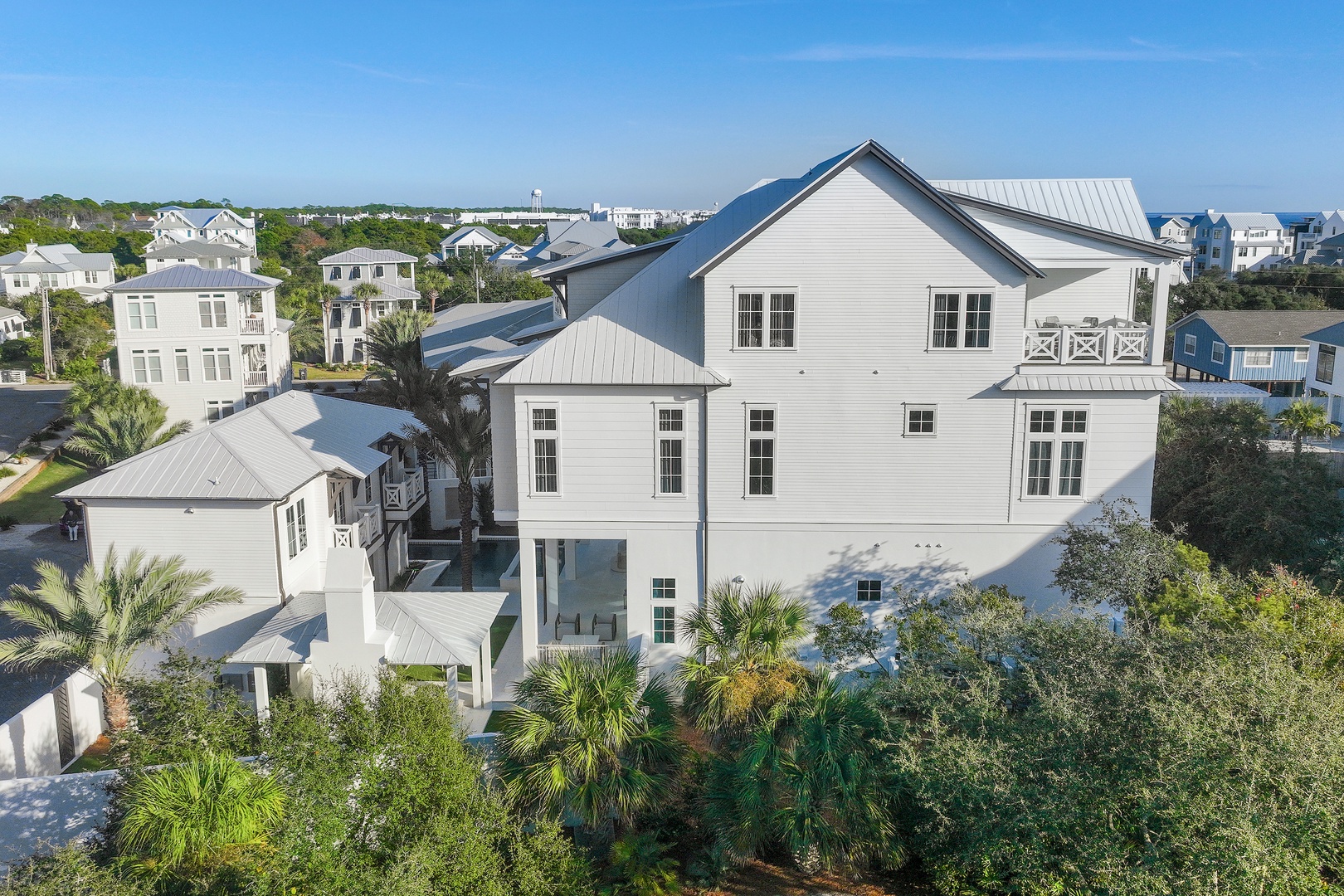 Modern coastal architecture situated in a serene beach community surrounded by palm trees and neighboring properties with ocean views in the distance.