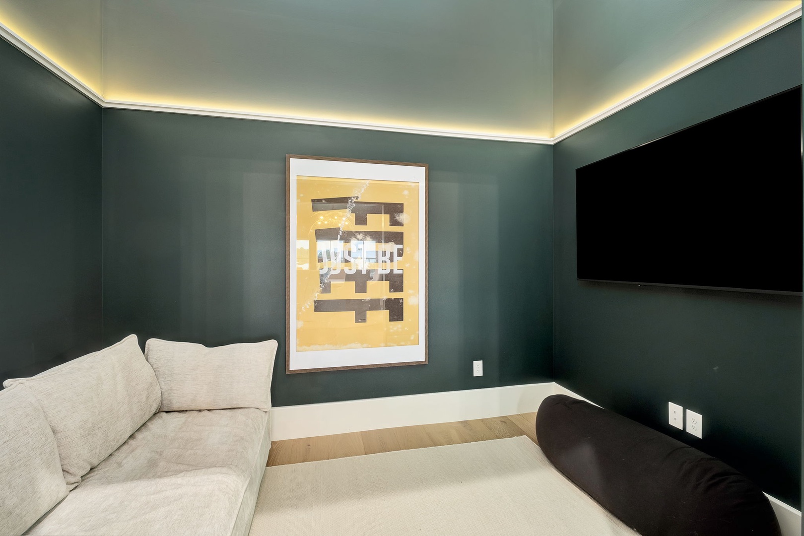 Sink into plush seating beneath soft ambient lighting in this cozy entertainment space. The dramatic teal walls and modern art create a sophisticated retreat perfect for your evening relaxation.