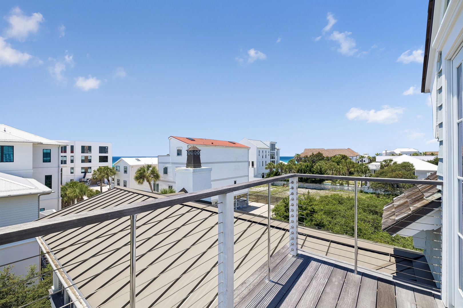 Private balcony overlooking coastal neighborhood with glimpses of the ocean and lush greenery. Bright, sunny day and modern railings frame the surrounding architecture and natural landscape.
