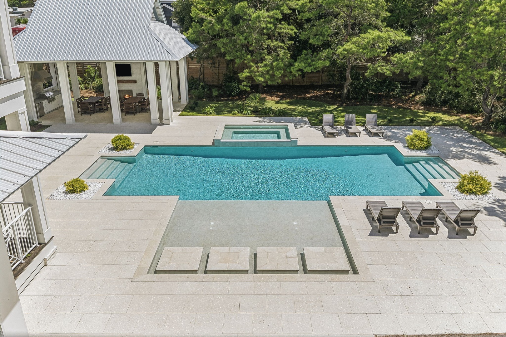 An aerial view of the property showcases a modern pool and hot tub set within a spacious patio area, surrounded by mature trees and manicured lawn.