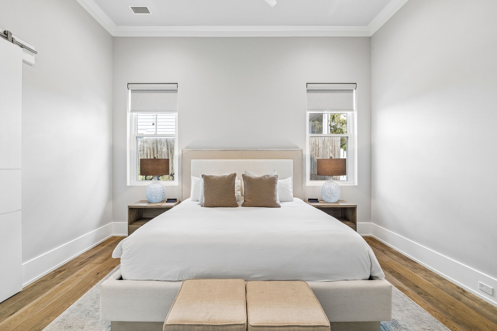 Wake up refreshed in your serene bedroom, featuring a plush bed framed by soft natural light streaming through dual windows. The warm wood floors and calming neutral tones create your perfect peaceful retreat.