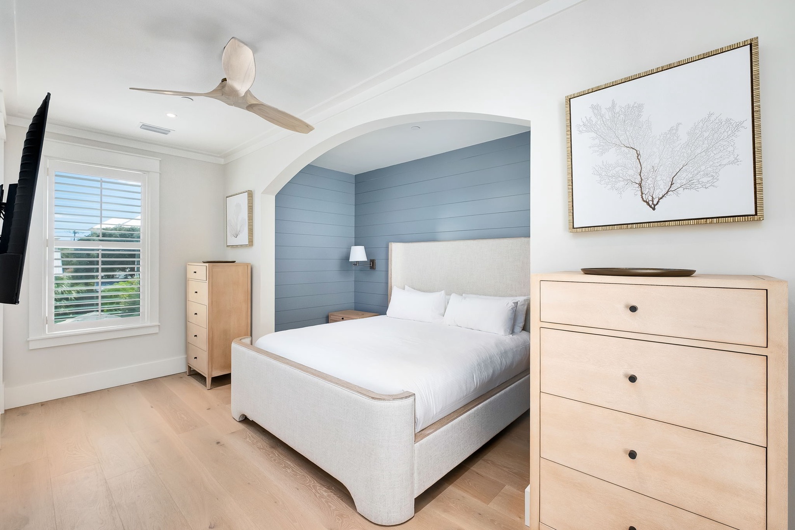 Drift off in this serene coastal-inspired bedroom, where the soft blue accent wall and natural wood tones create your perfect retreat. Wake to gentle breezes from the ceiling fan above your plush queen bed.
