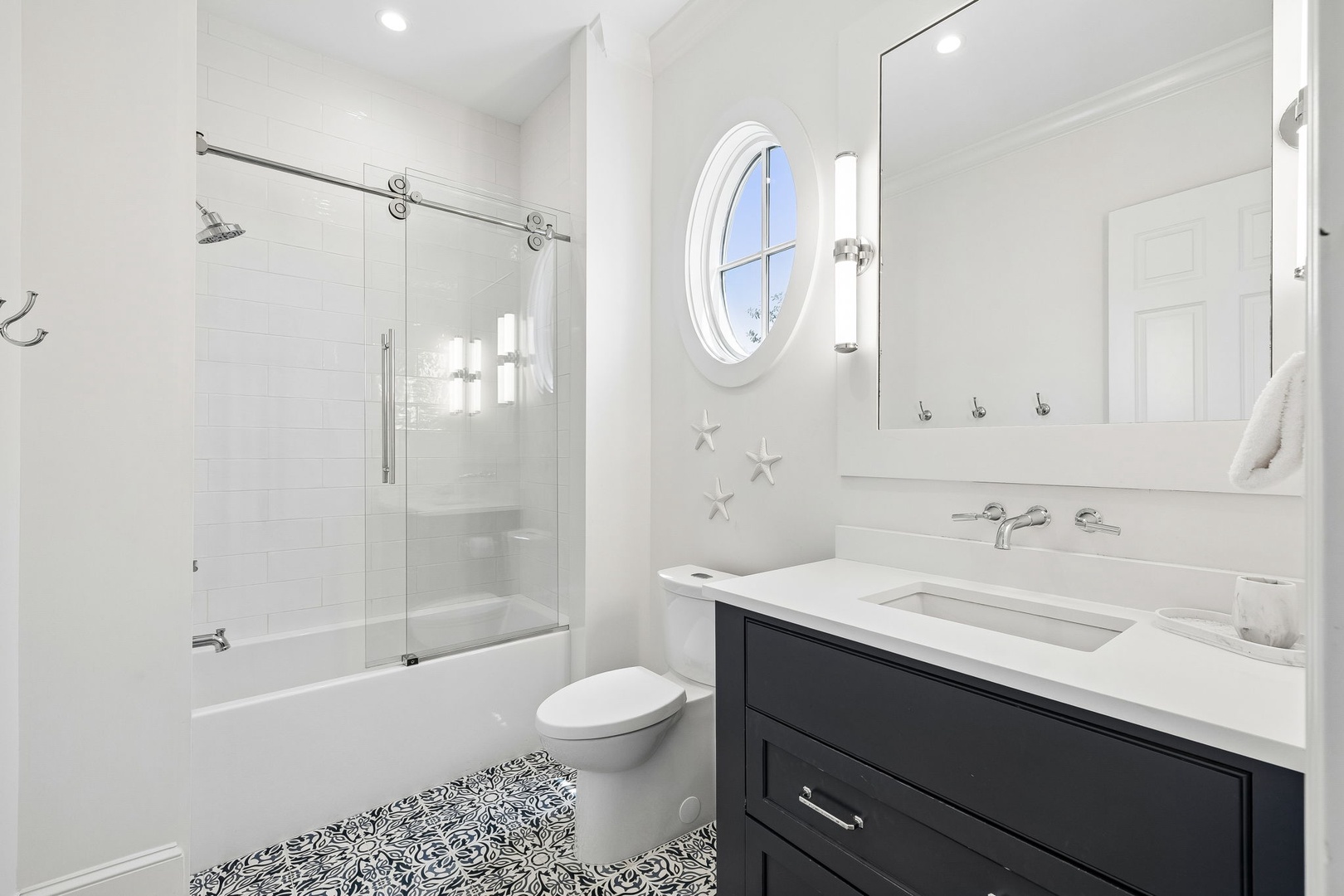 Freshen up in your pristine private bathroom, featuring bright white tile, a sleek vanity, and nautical starfish accents adding coastal charm. A relaxing soak awaits in the tub-shower combo.