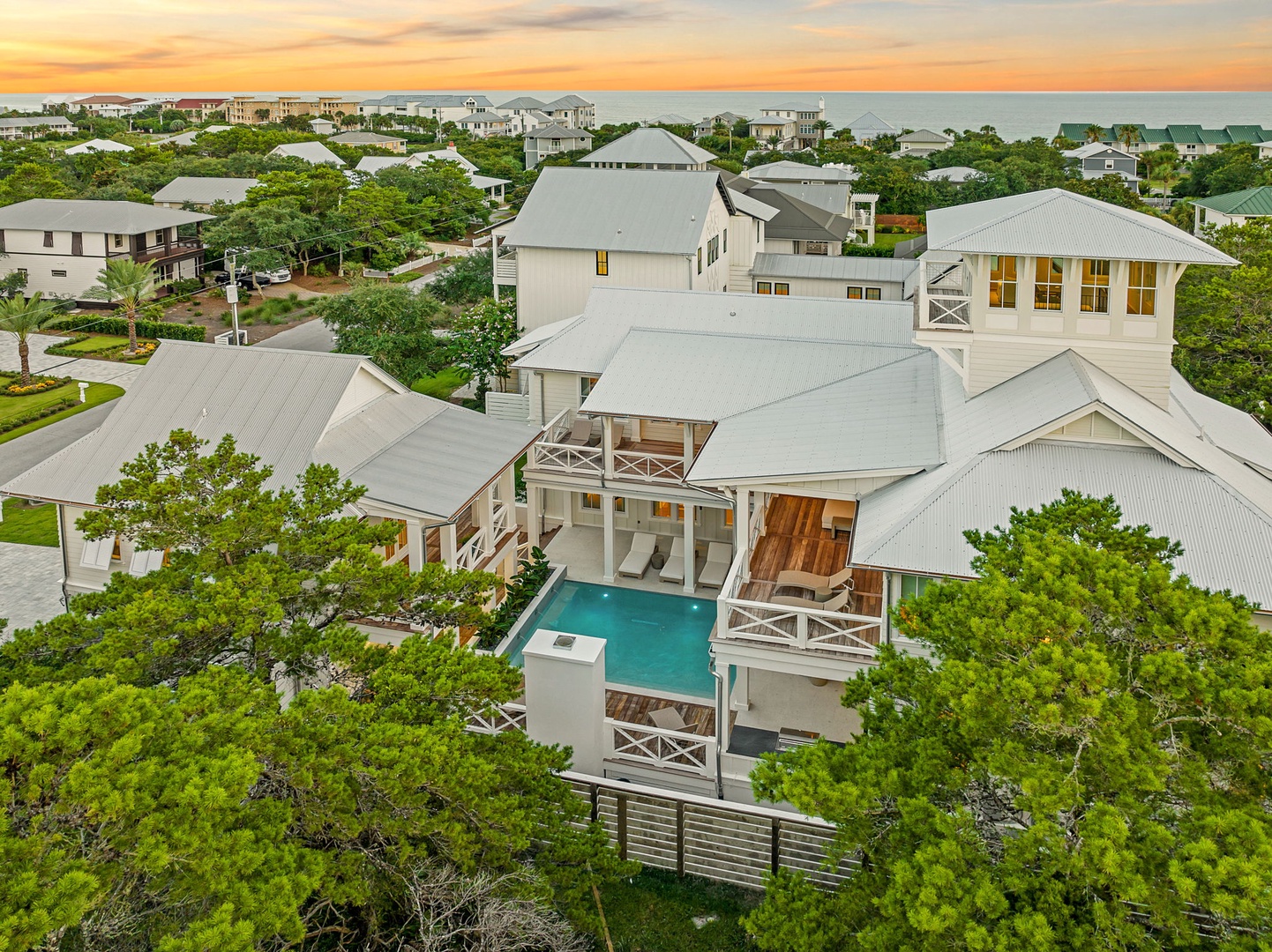 Aerial view of this coastal property at golden hour, showcasing the private pool, multiple balconies, and convenient proximity to both the beach and charming neighborhood amenities.
