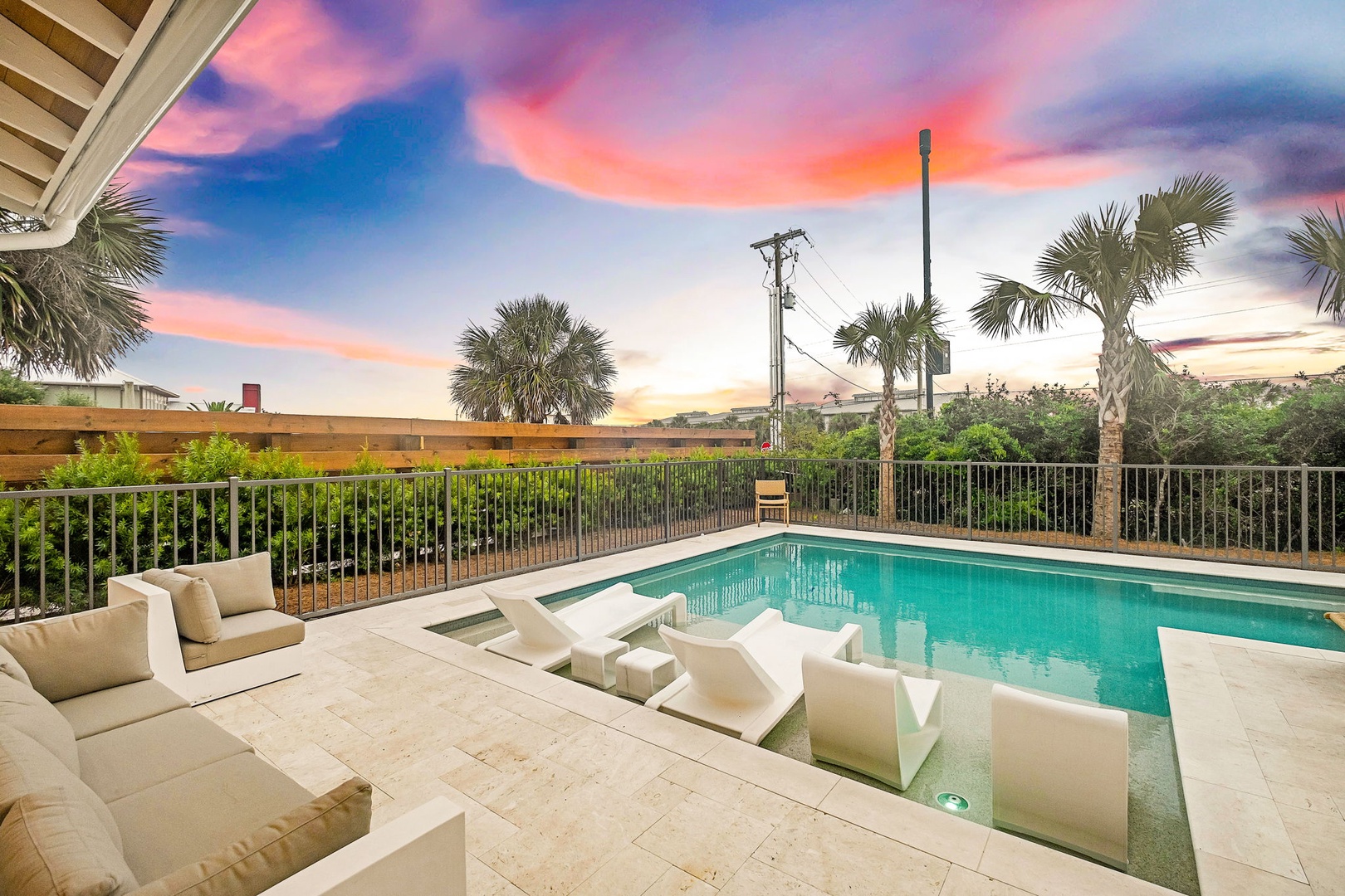 Private pool area with modern lounge furniture set against a backdrop of swaying palms and colorful coastal skies, providing an ideal space to unwind after beach days.