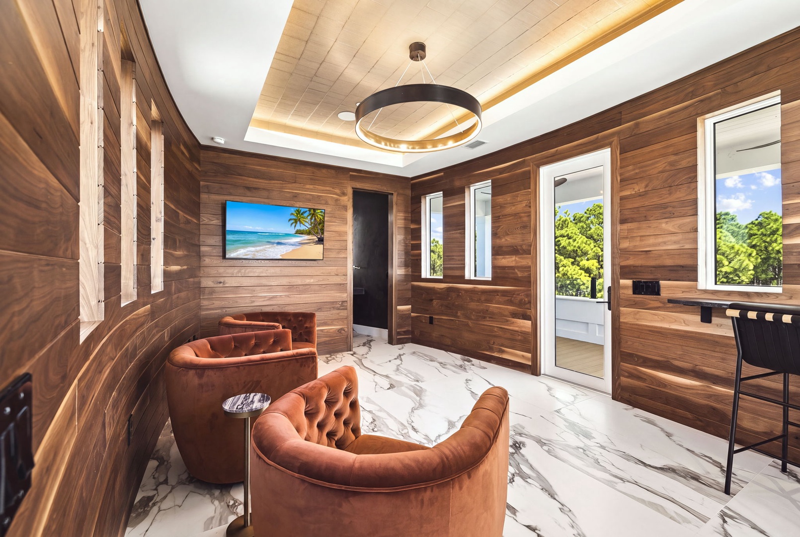 Settle into plush velvet seating under warm wood tones and modern lighting. French doors open to your private outdoor space with lush views beyond.