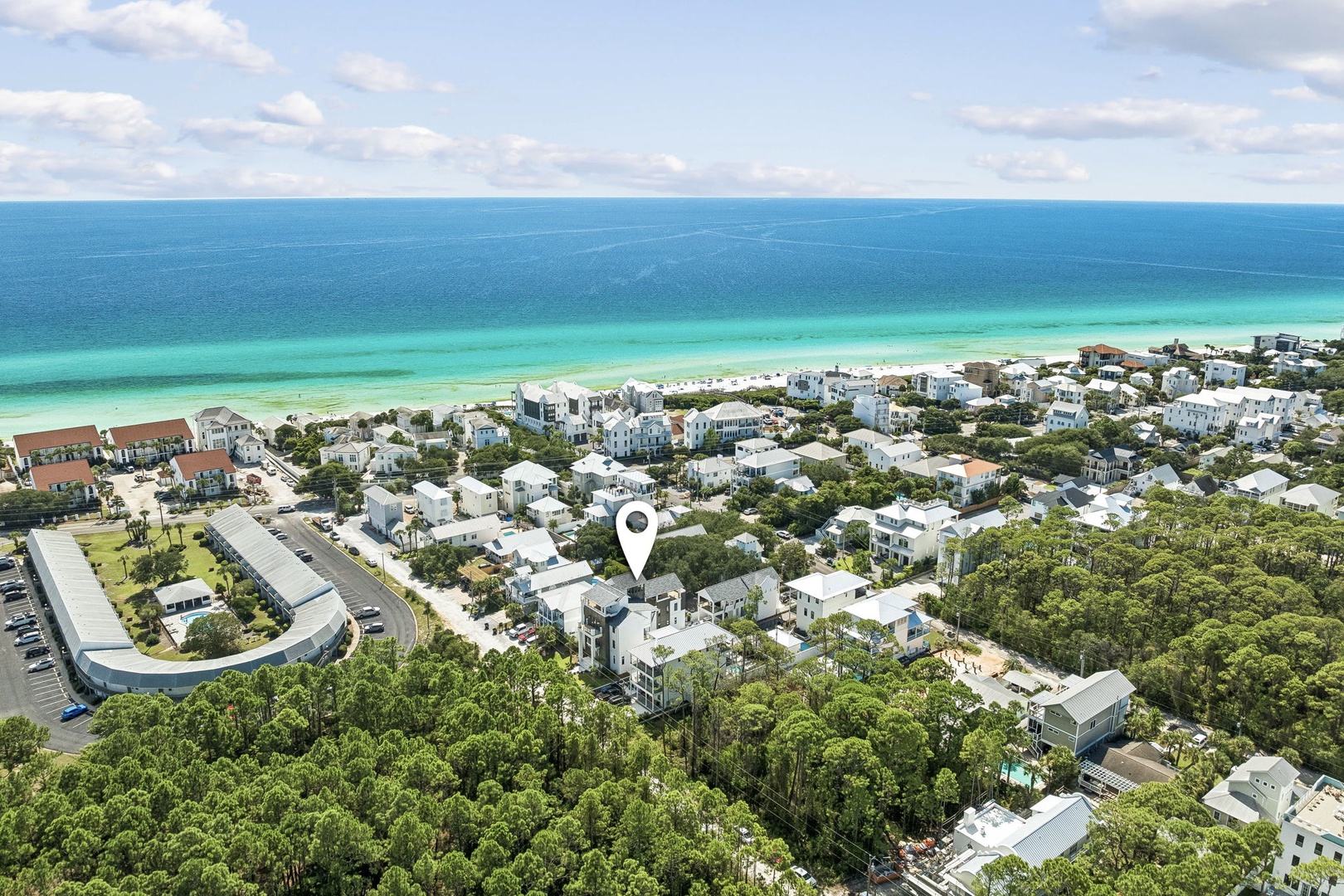 Aerial view of a coastal community nestled among lush greenery, with pristine white sand beaches and turquoise Gulf waters stretching to the horizon.